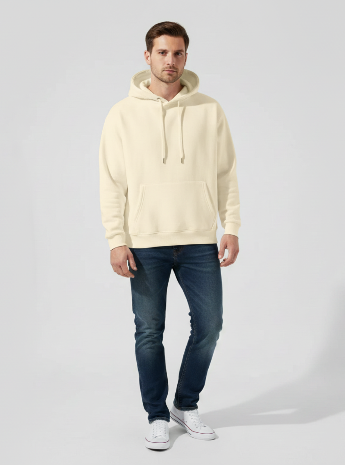 Man wearing a beige hoodie and blue jeans on a white background