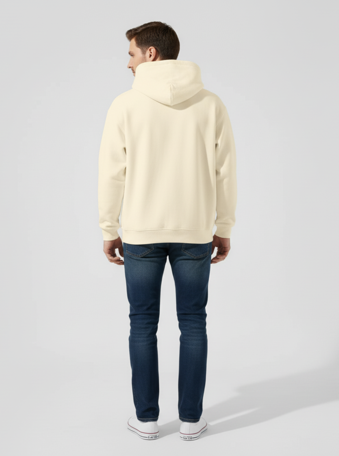 Person wearing a beige hoodie and dark jeans on a light gray background