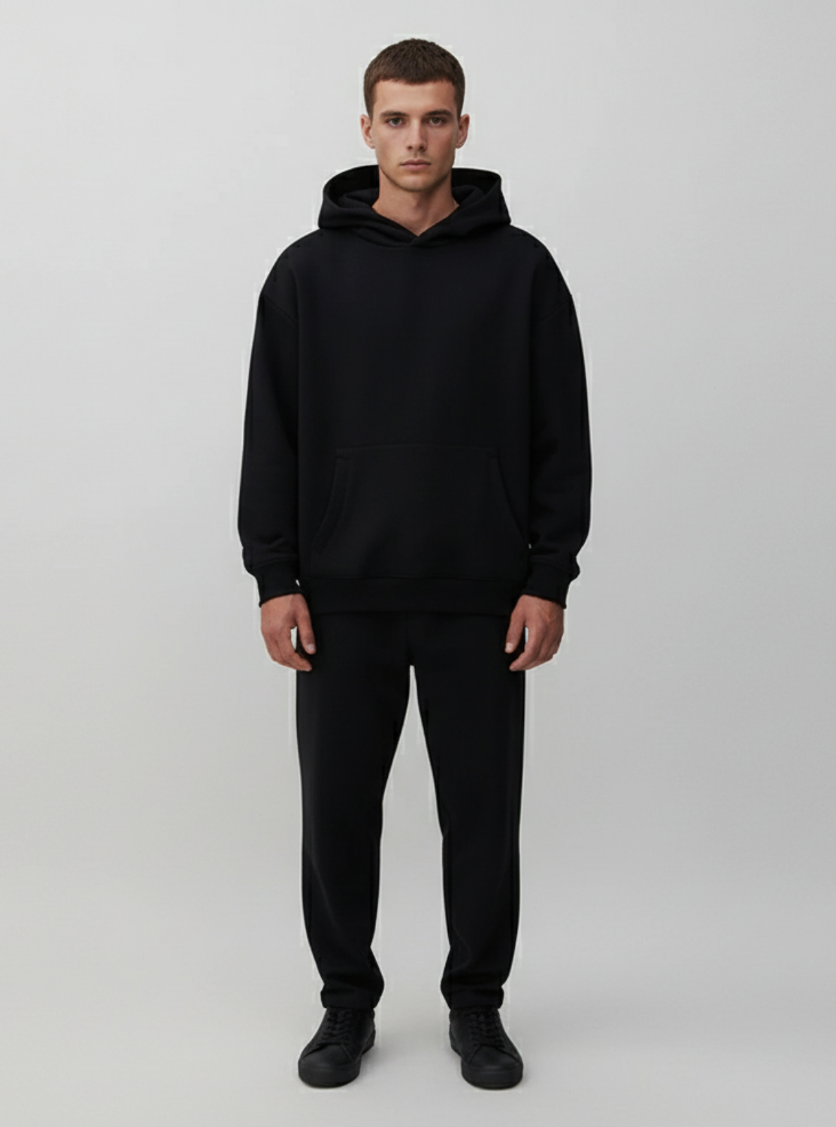 Man wearing a black hoodie and pants on a light gray background