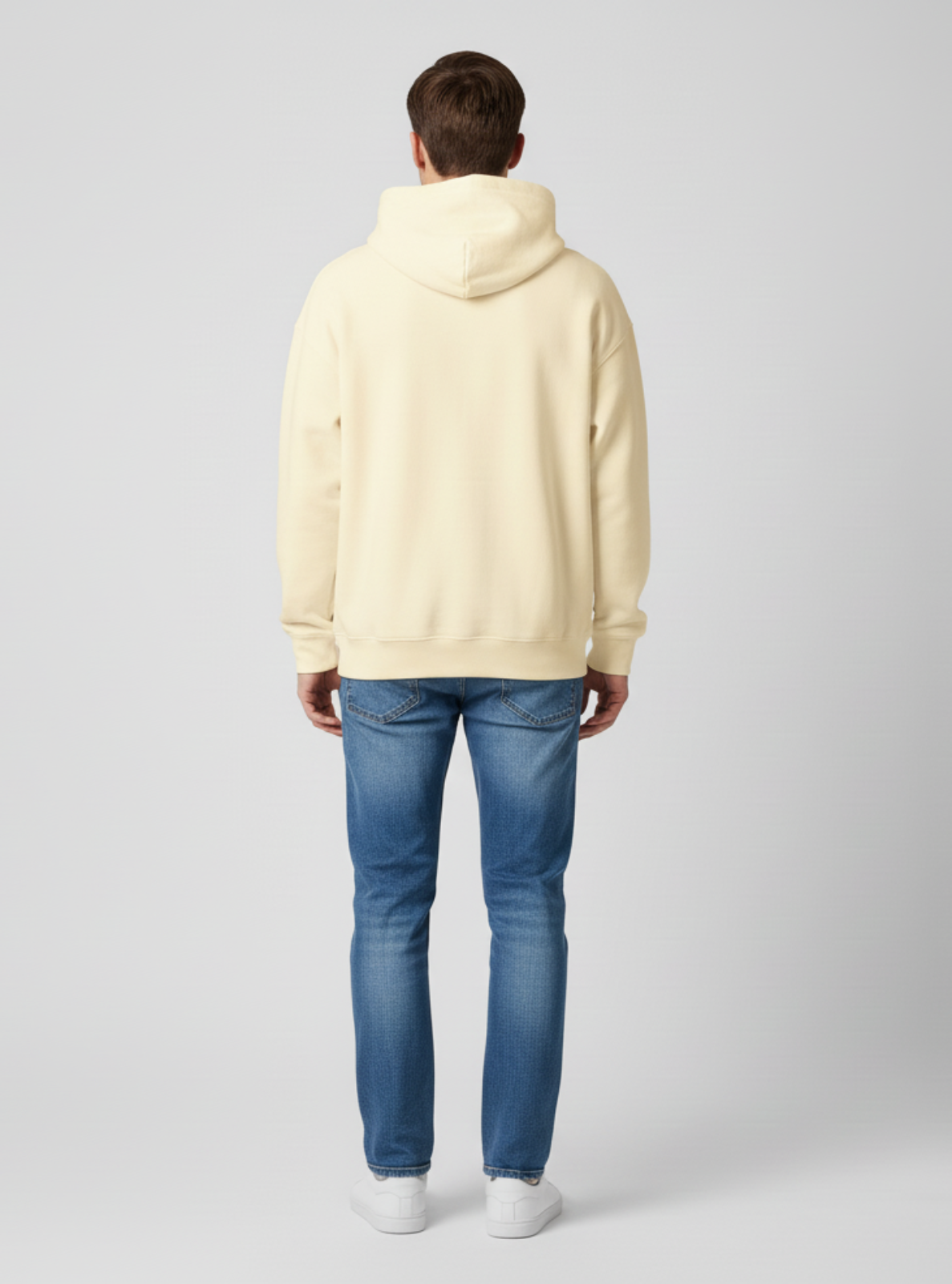Person wearing a light-colored hoodie and blue jeans on a plain background