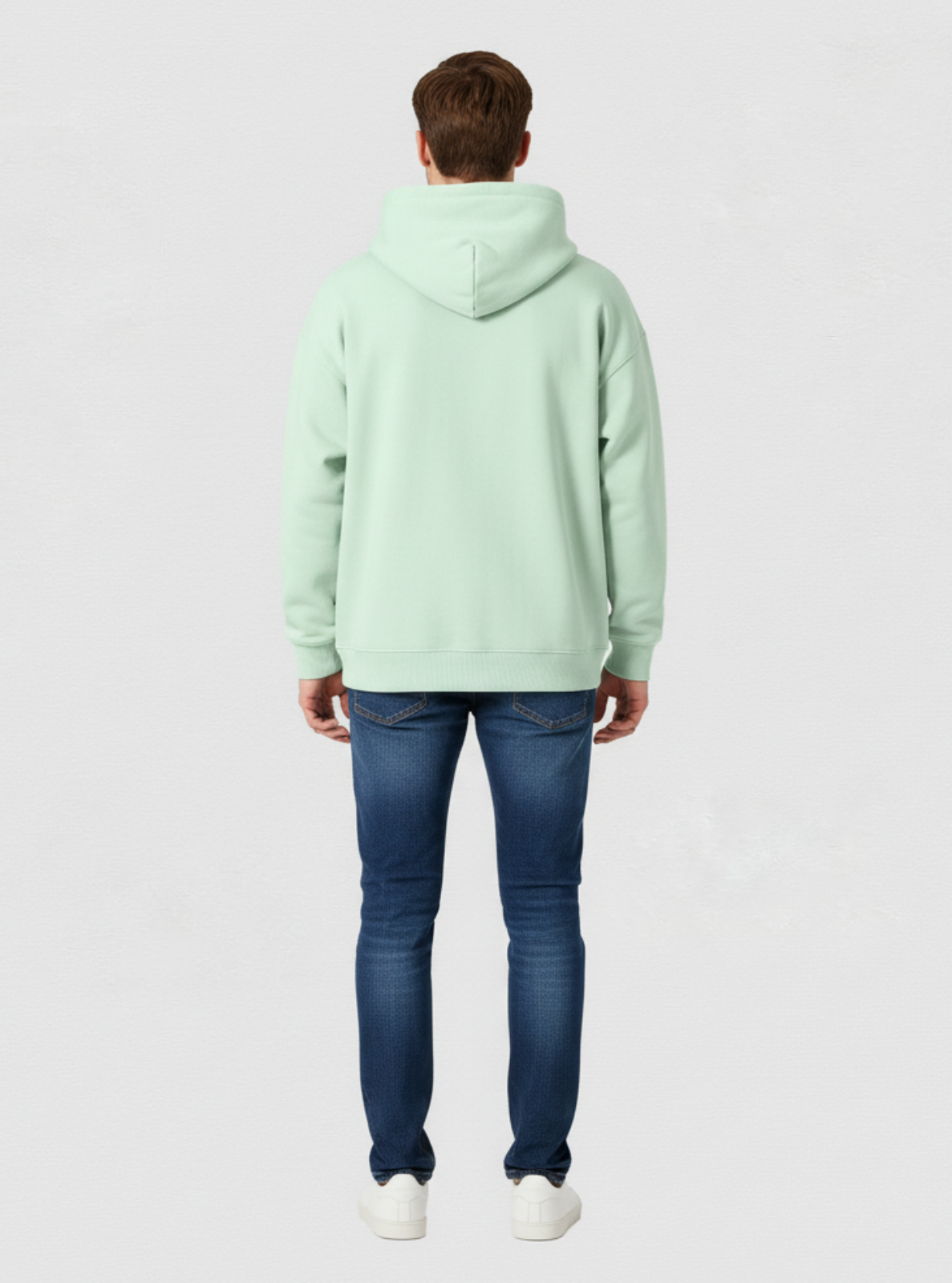 Person wearing a light green hoodie and blue jeans on a white background