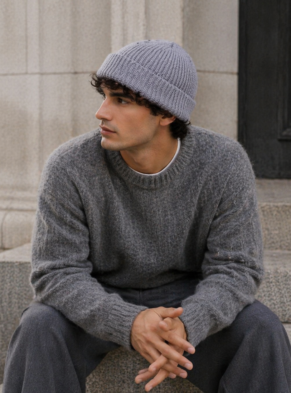 Man wearing a gray knit sweater and beanie sitting on steps.