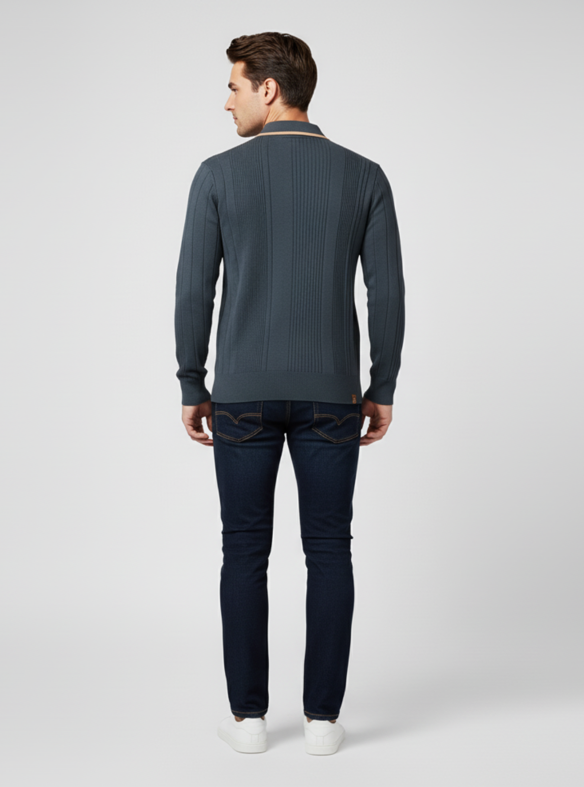 Man wearing a gray ribbed sweater and dark jeans on a light gray background