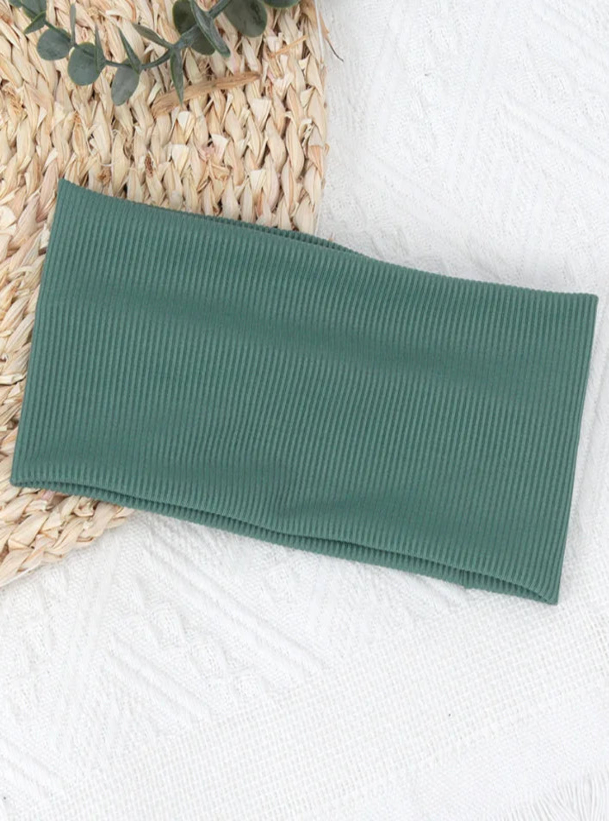 Green ribbed towel on a textured surface with a woven mat and plant leaves.