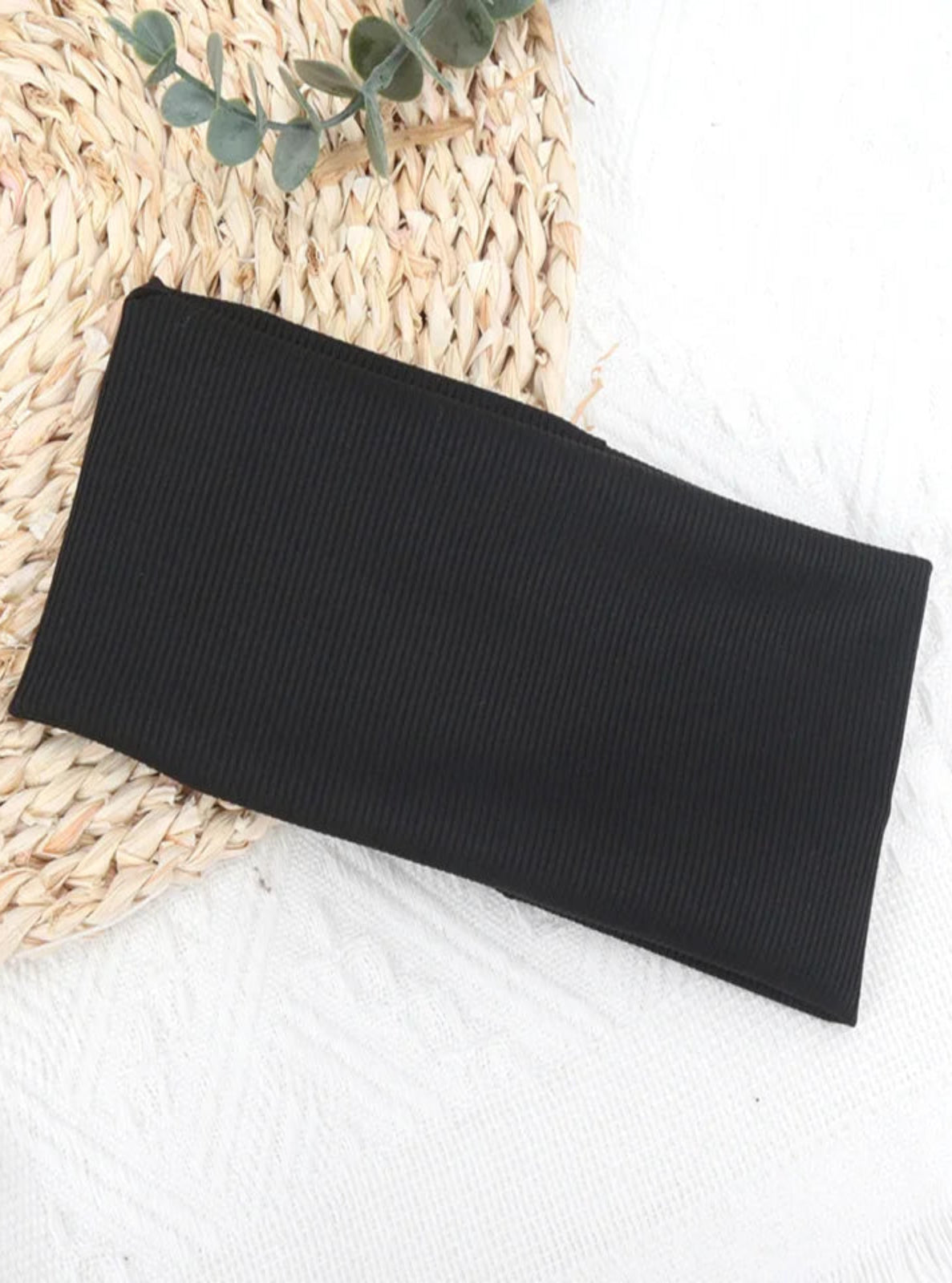 Black ribbed knit headband on a textured surface with green leaves.