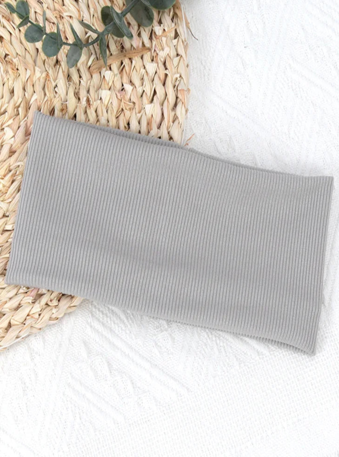 Gray ribbed Rib-Knit Stretch Headband on a textured surface with a woven mat and green leaves.