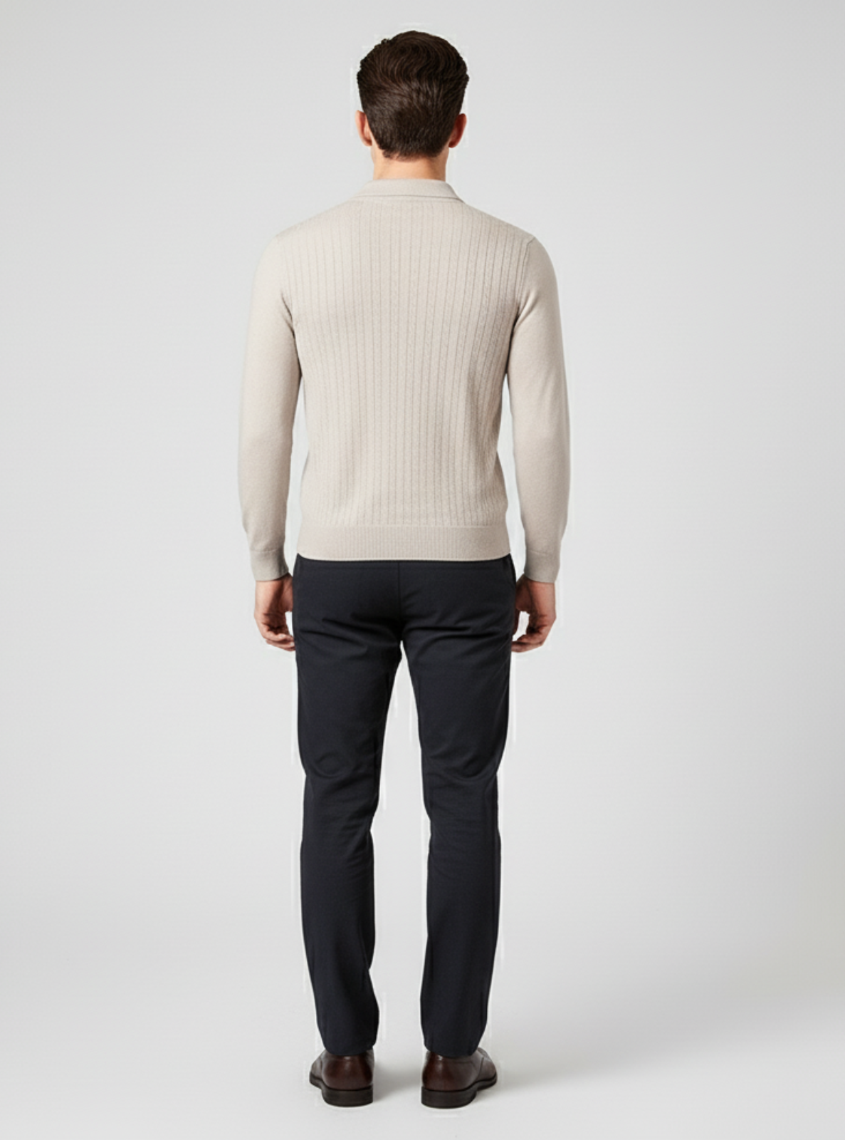 Man wearing a beige sweater and dark pants on a white background