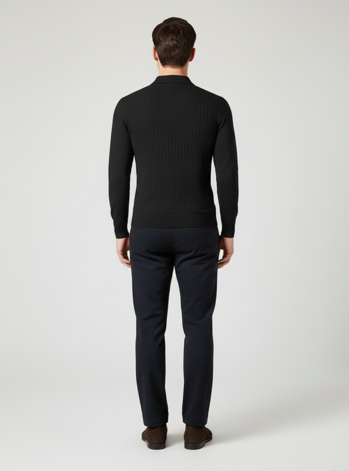 Man wearing a black ribbed sweater and dark pants on a white background