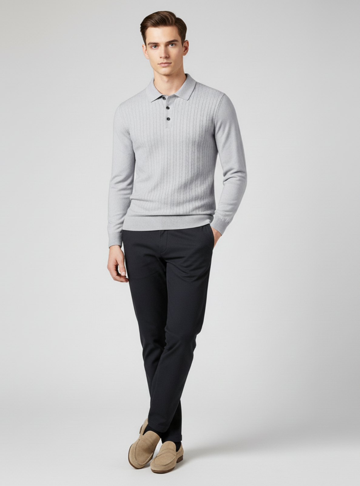 Man wearing a light gray sweater over a polo shirt with dark pants on a white background