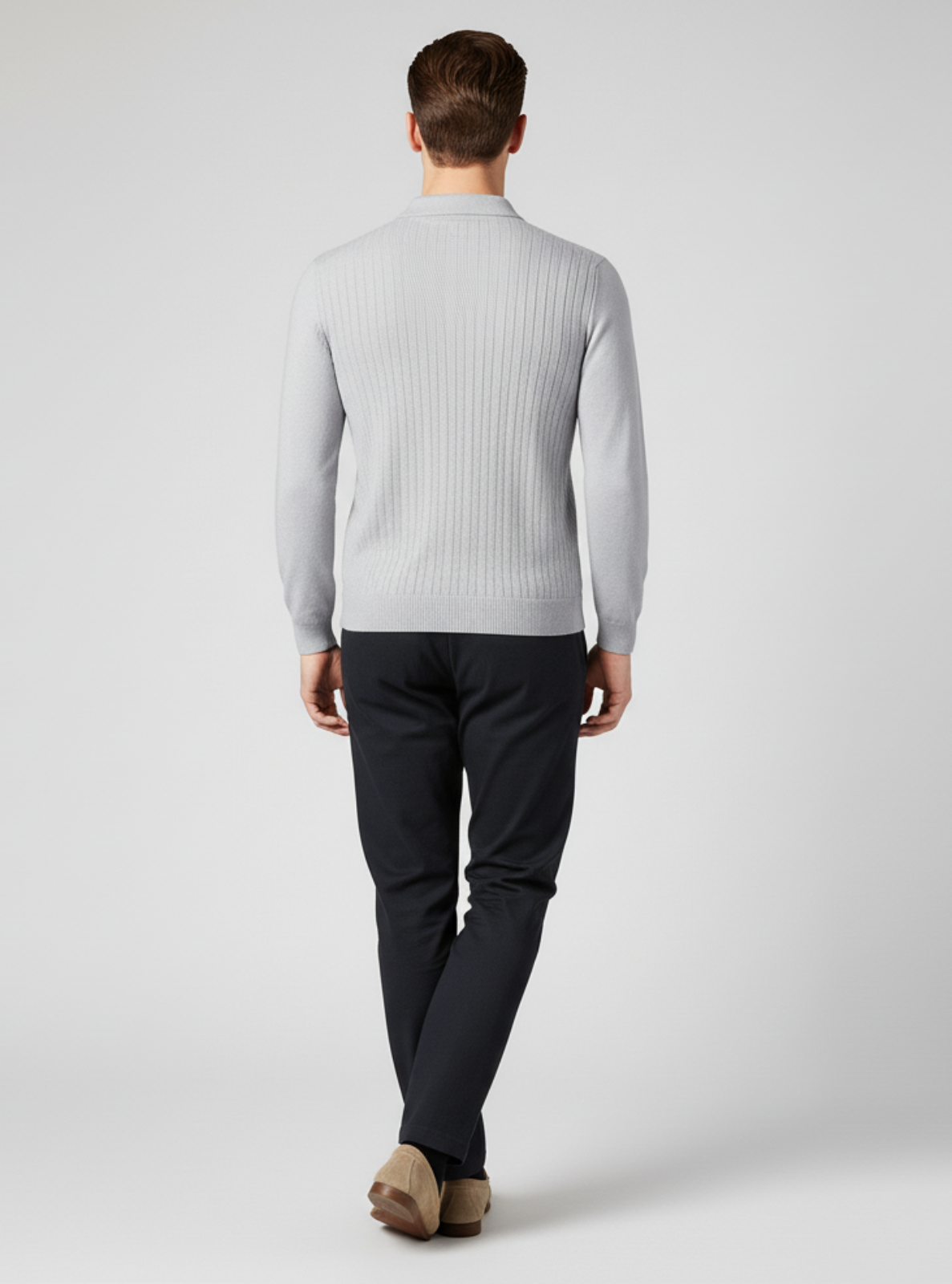 Man wearing a light gray ribbed sweater and dark pants on a white background