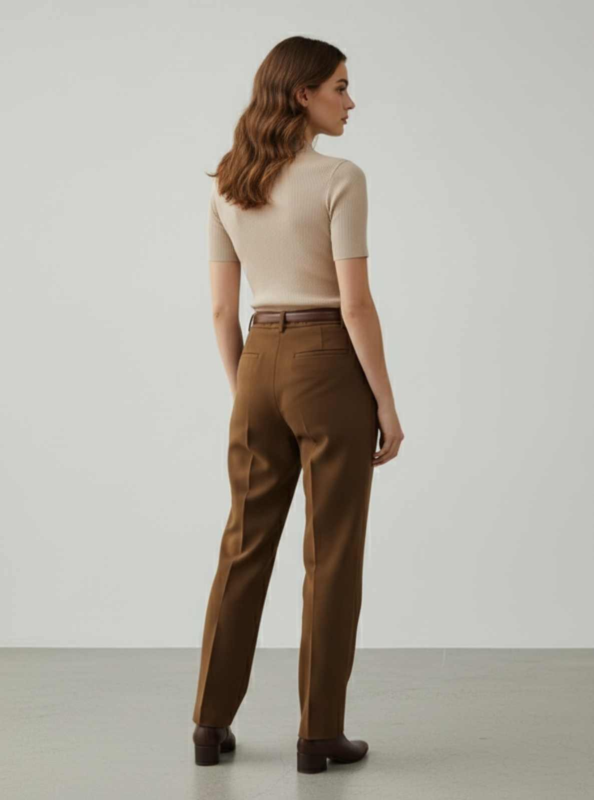 Woman wearing brown pants and a beige top against a plain background