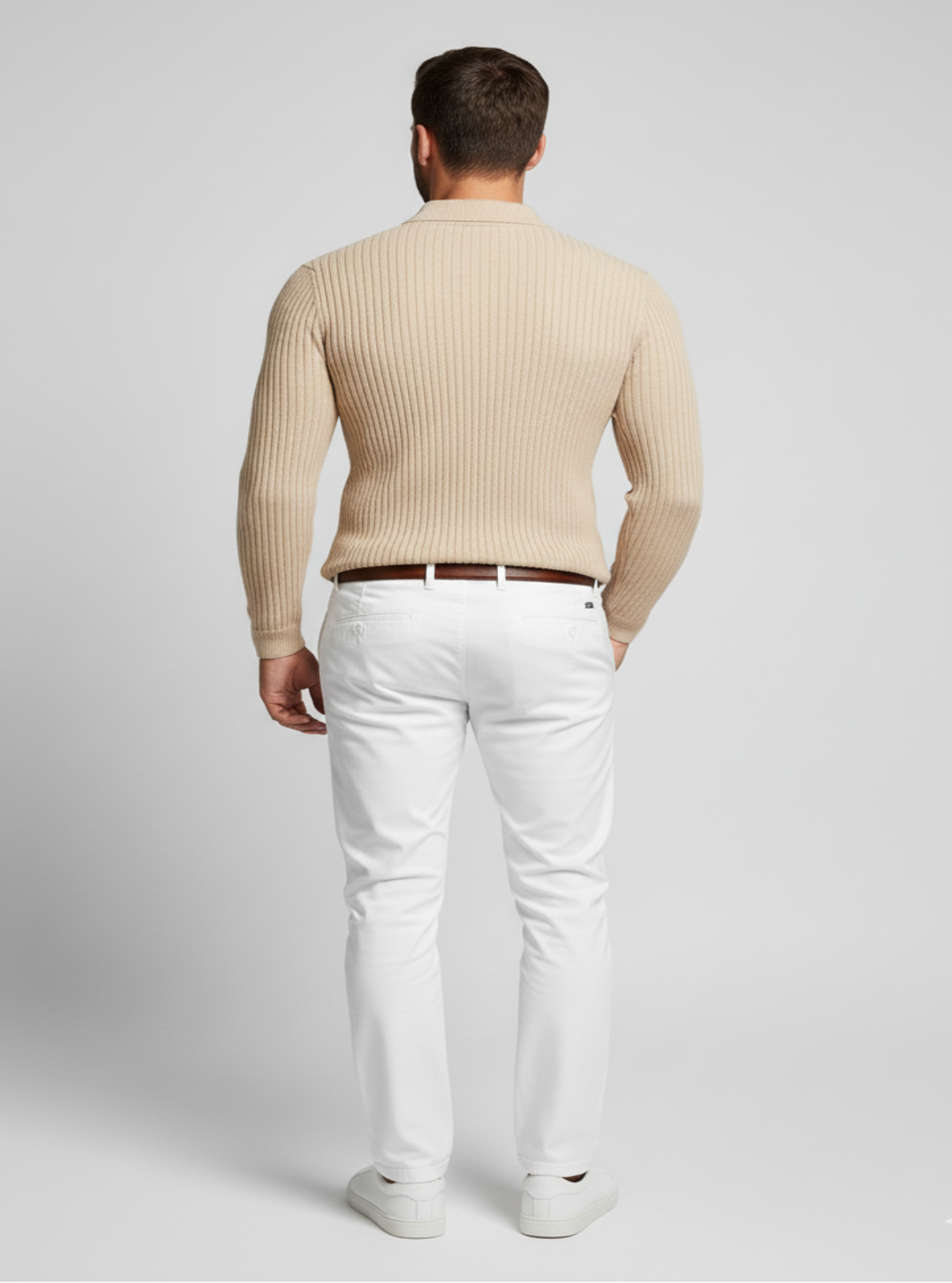 Man wearing a beige ribbed sweater and white pants on a light gray background