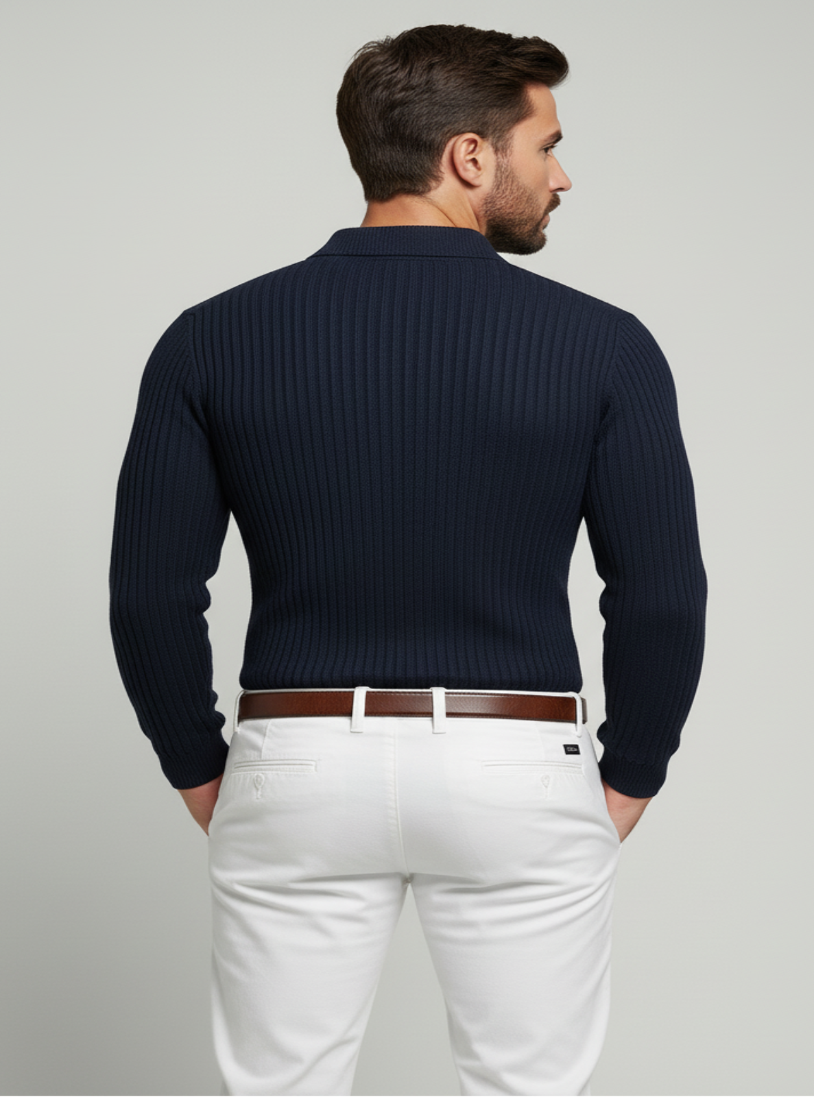Man wearing a navy ribbed sweater and white pants on a light gray background