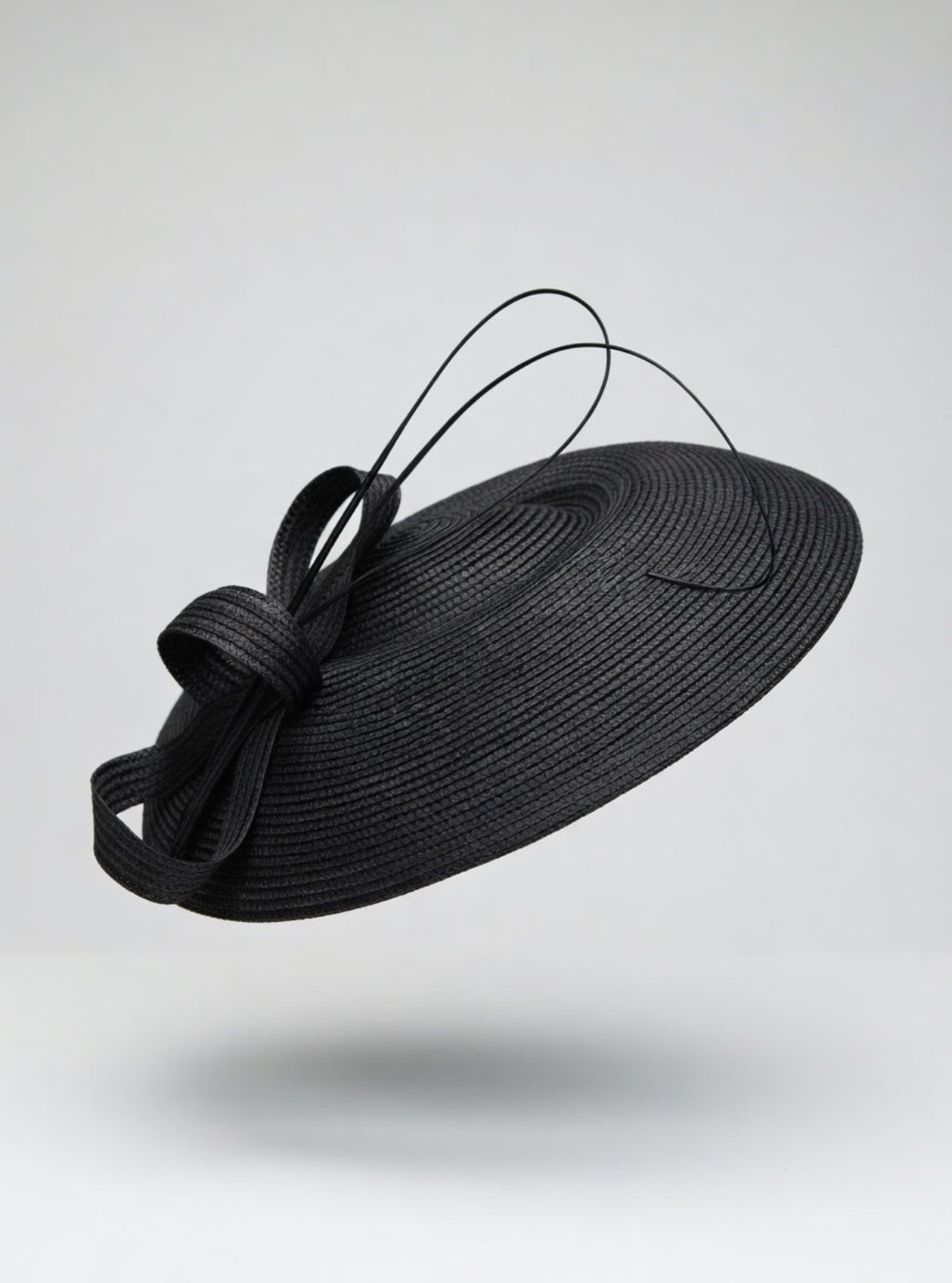 Black straw hat with a decorative bow on a light gray background