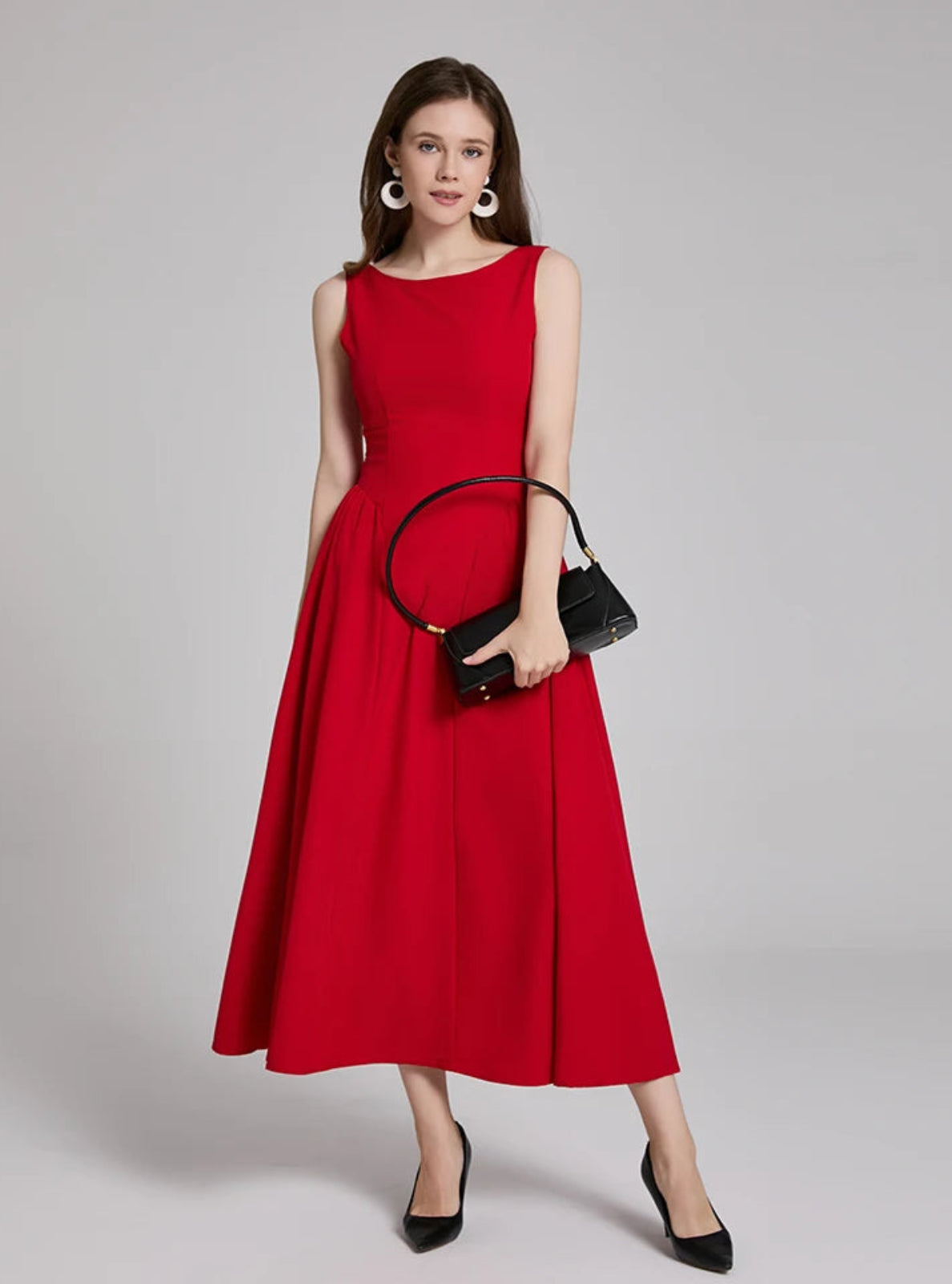 Woman wearing a red dress holding a black handbag on a gray background