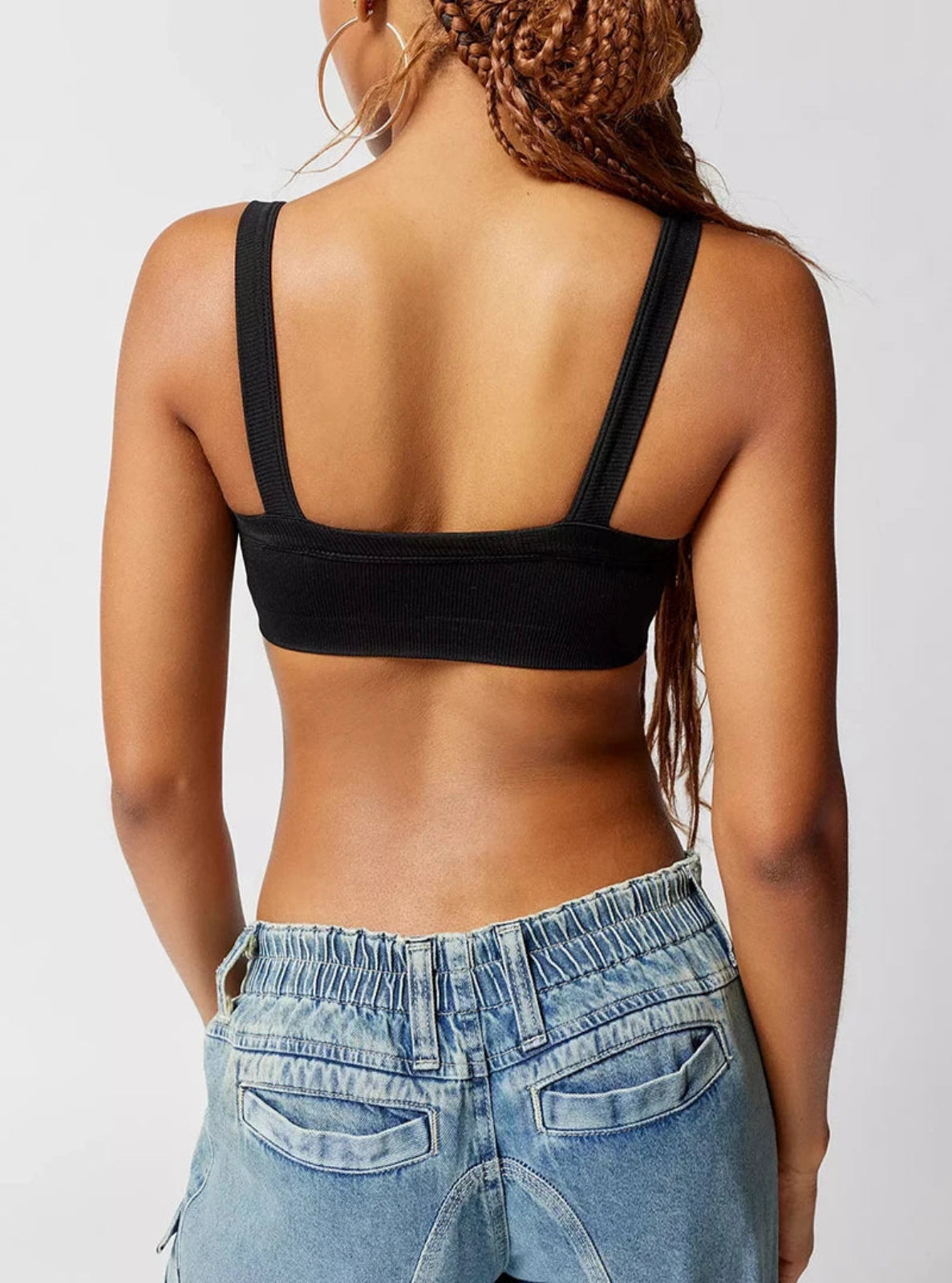 Person wearing a black crop top and blue jeans on a plain background