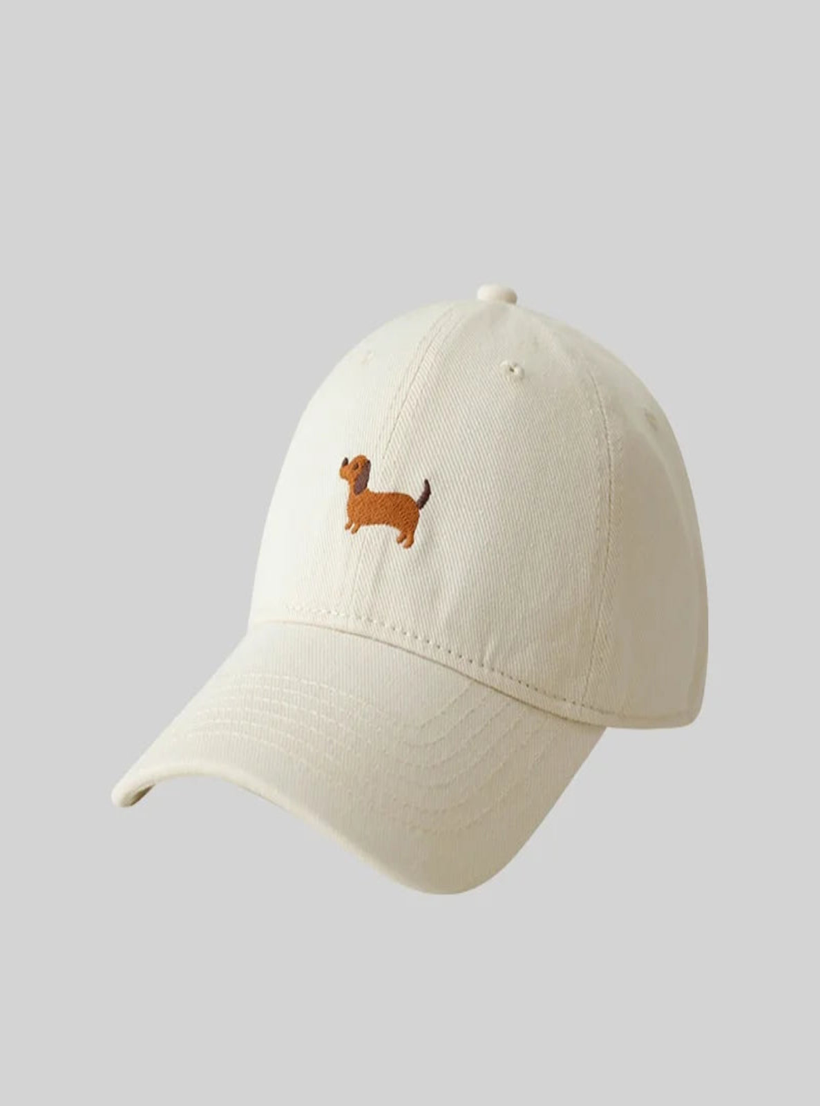 Cream cap with a small embroidered dog design on a light gray background