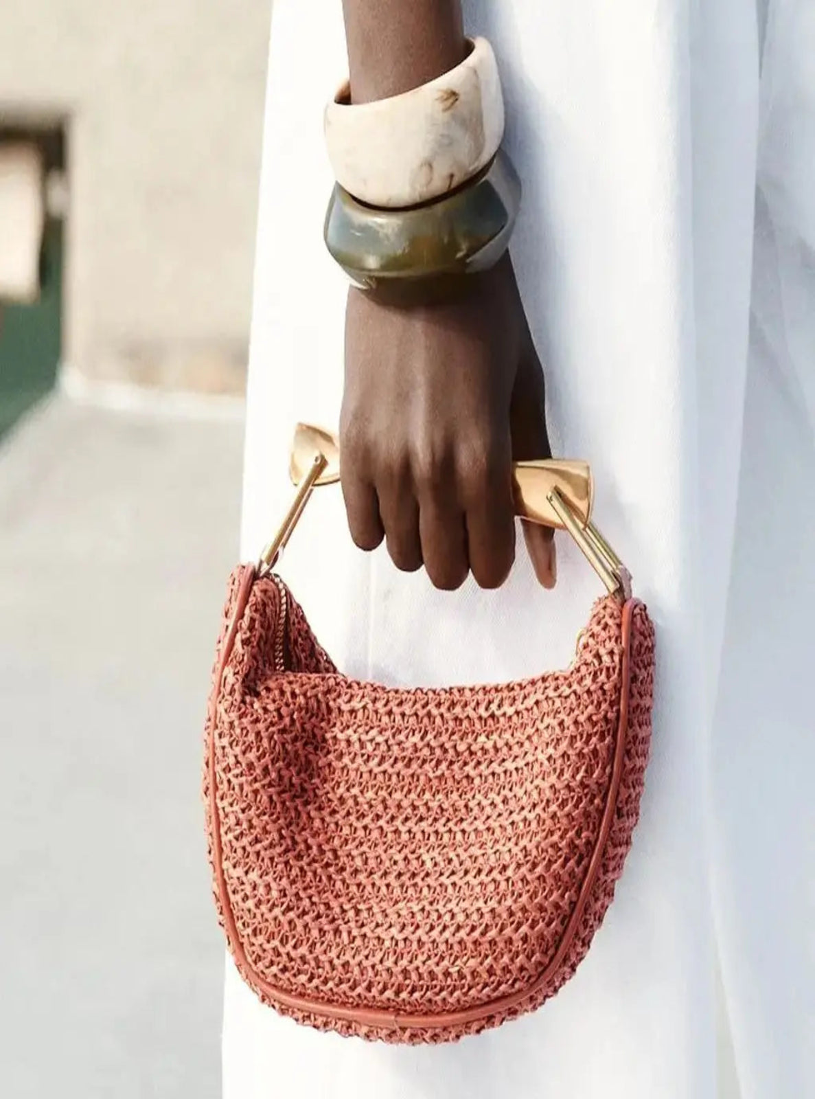 Person holding a red woven handbag with gold handles against a blurred background