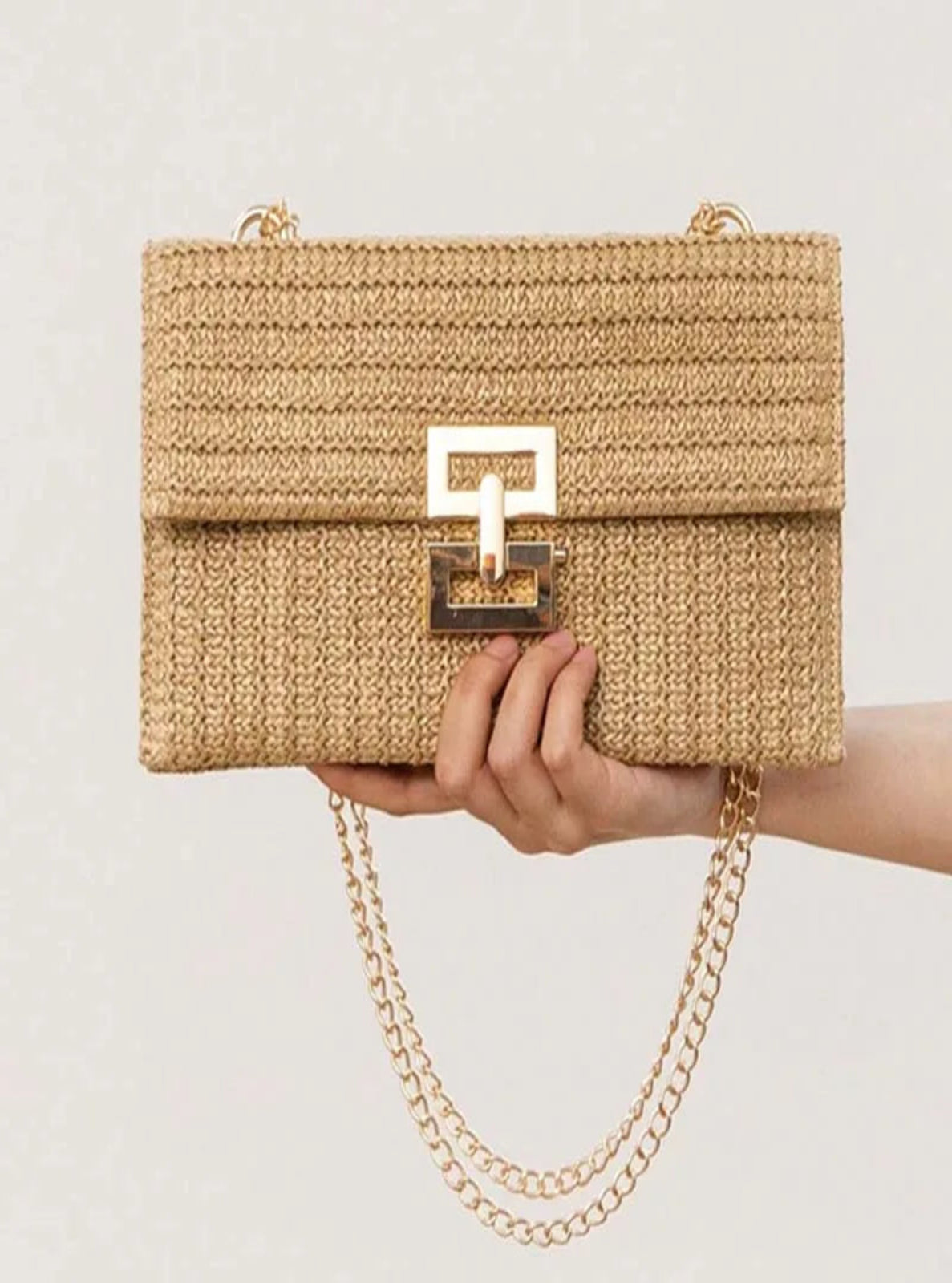 Woven handbag with a chain strap held by a hand against a light background