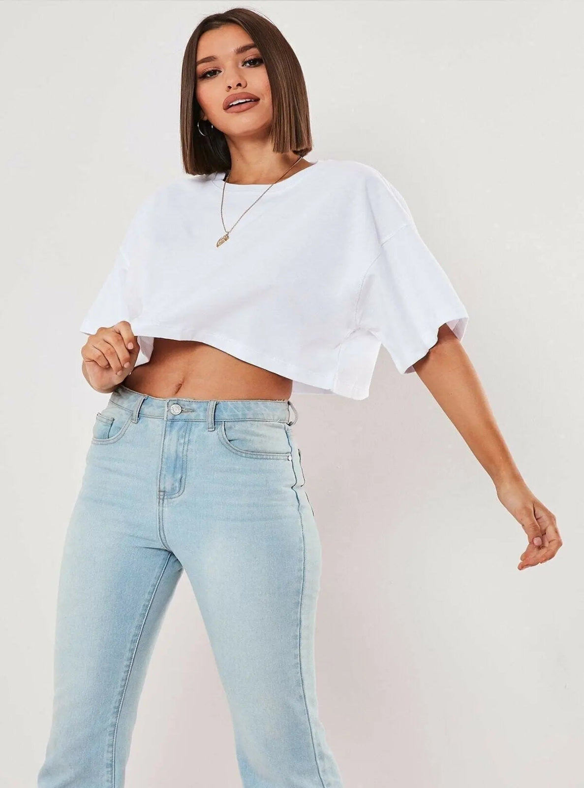 Person wearing a white cropped top and light blue jeans on a plain background