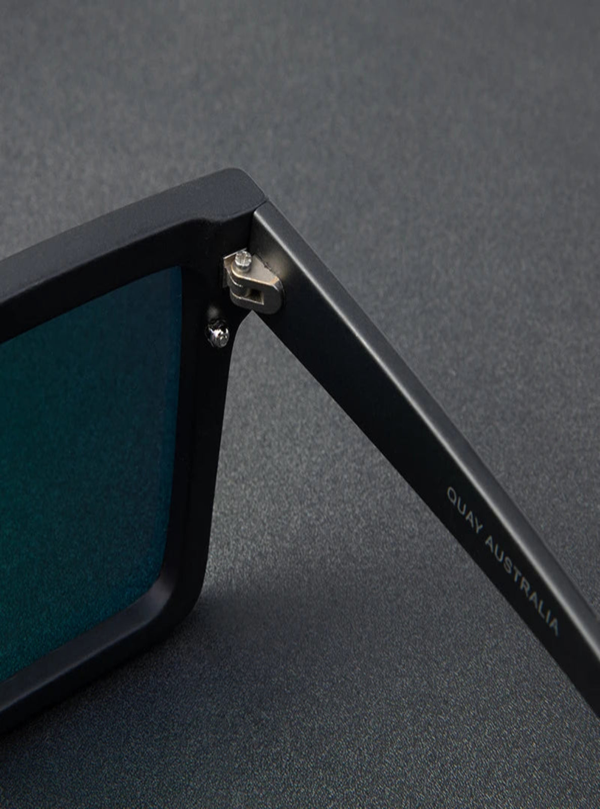 Close-up of a black Quay Australia sunglasses frame on a gray background