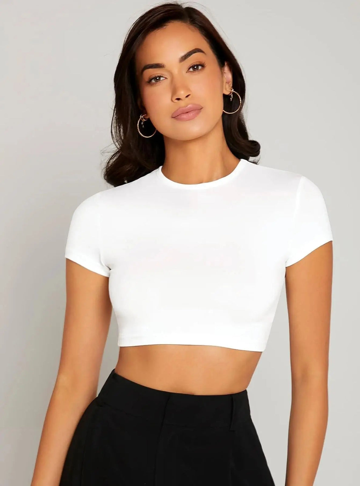 Woman wearing a white crop top against a plain background