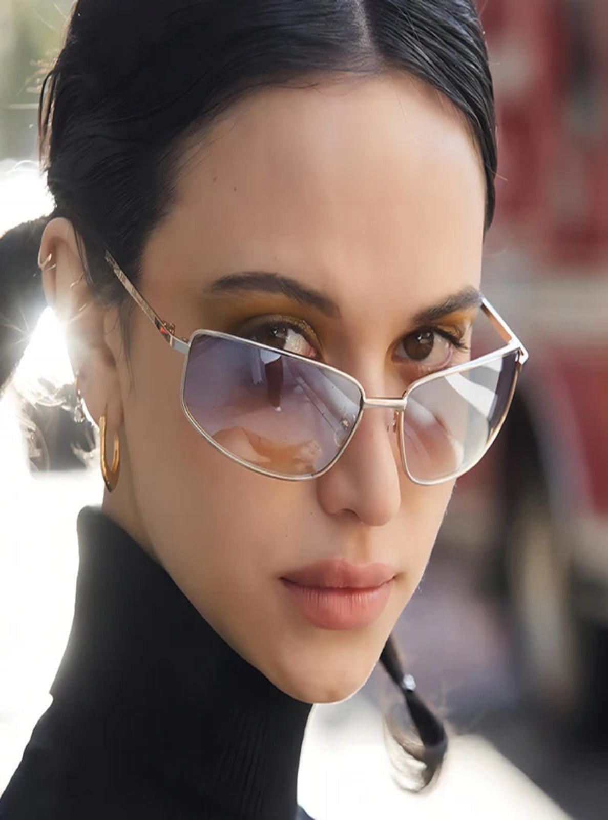 Close-up of a person wearing cat-eye sunglasses with a blurred background