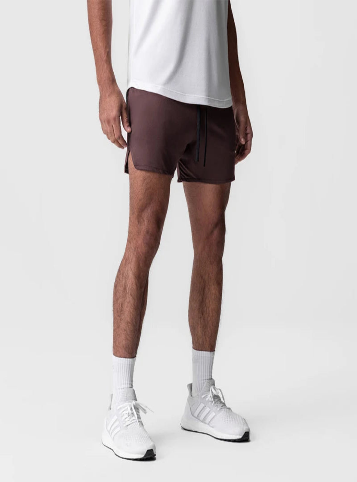 Person wearing brown shorts, white shirt, white socks, and white sneakers on a light gray background