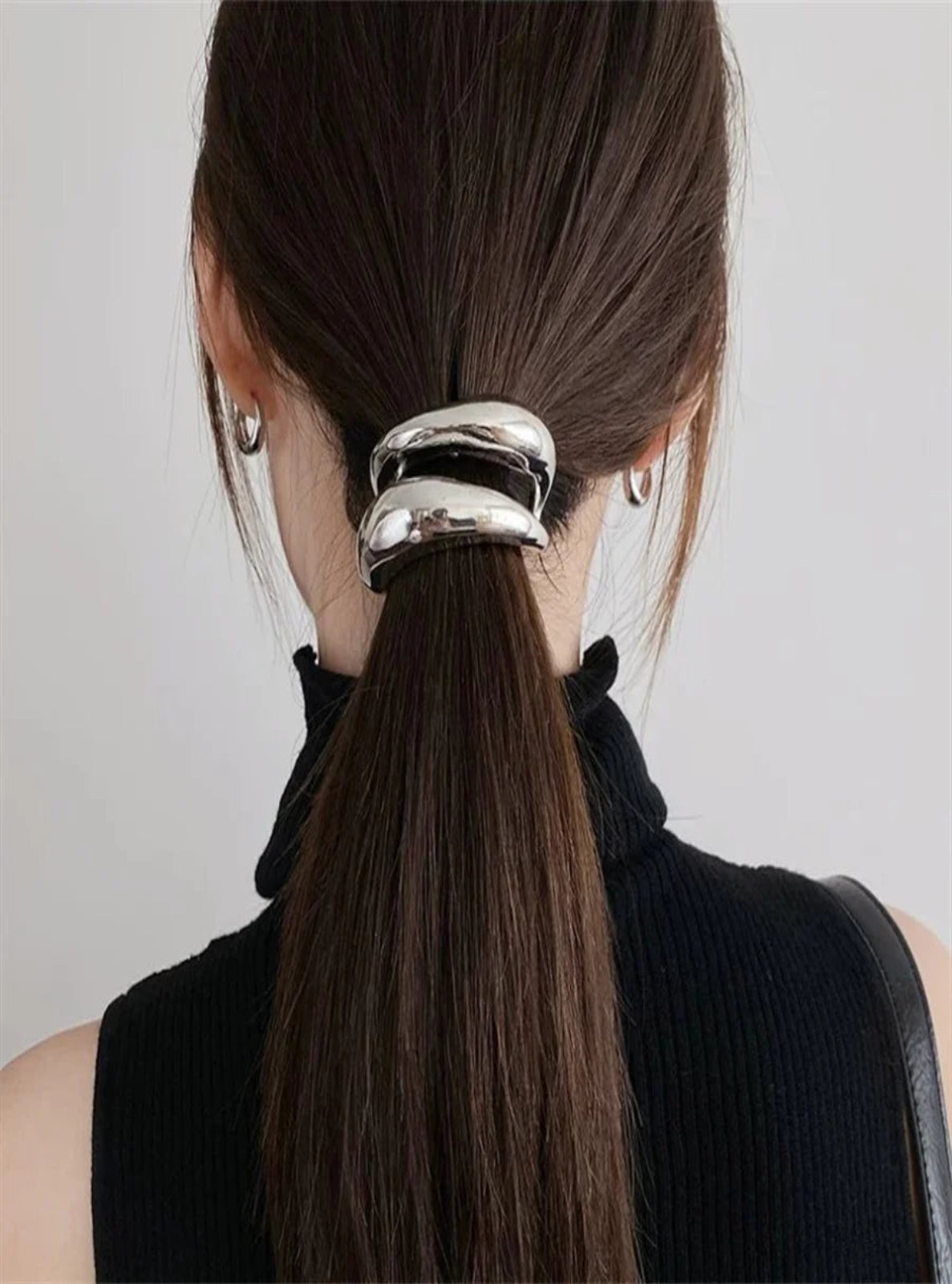 Person with a ponytail held by a silver hair tie against a plain background