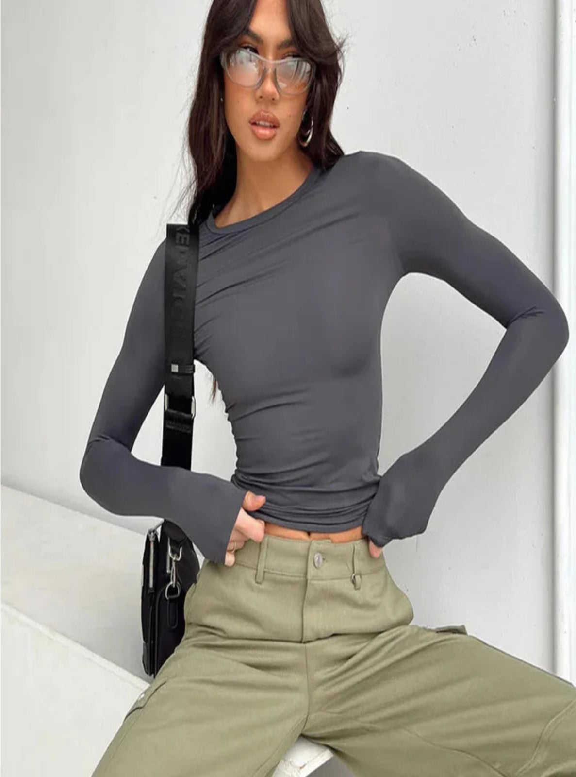 Woman wearing a gray long-sleeve top and green pants against a white background