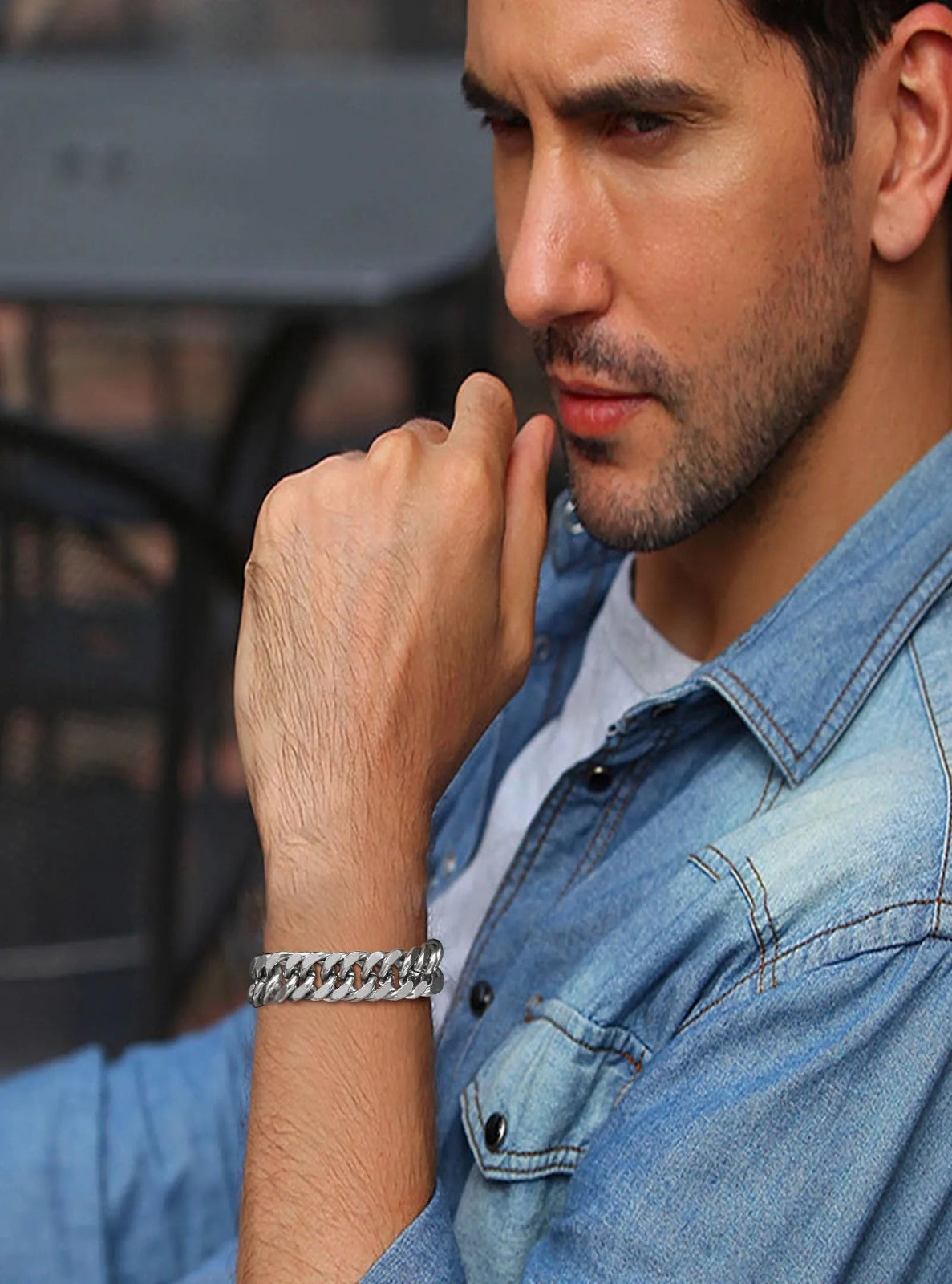 Man wearing a silver bracelet, wearing a denim shirt, with a blurred background