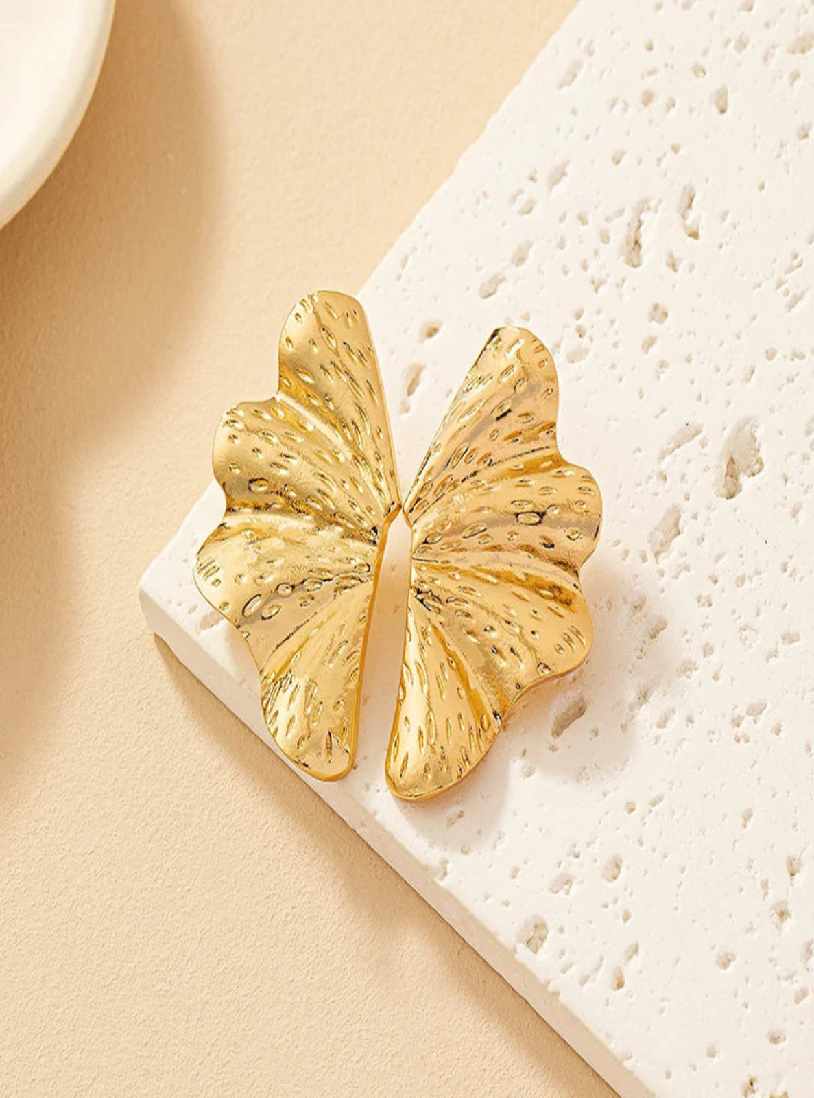 Gold earring on a textured white surface.