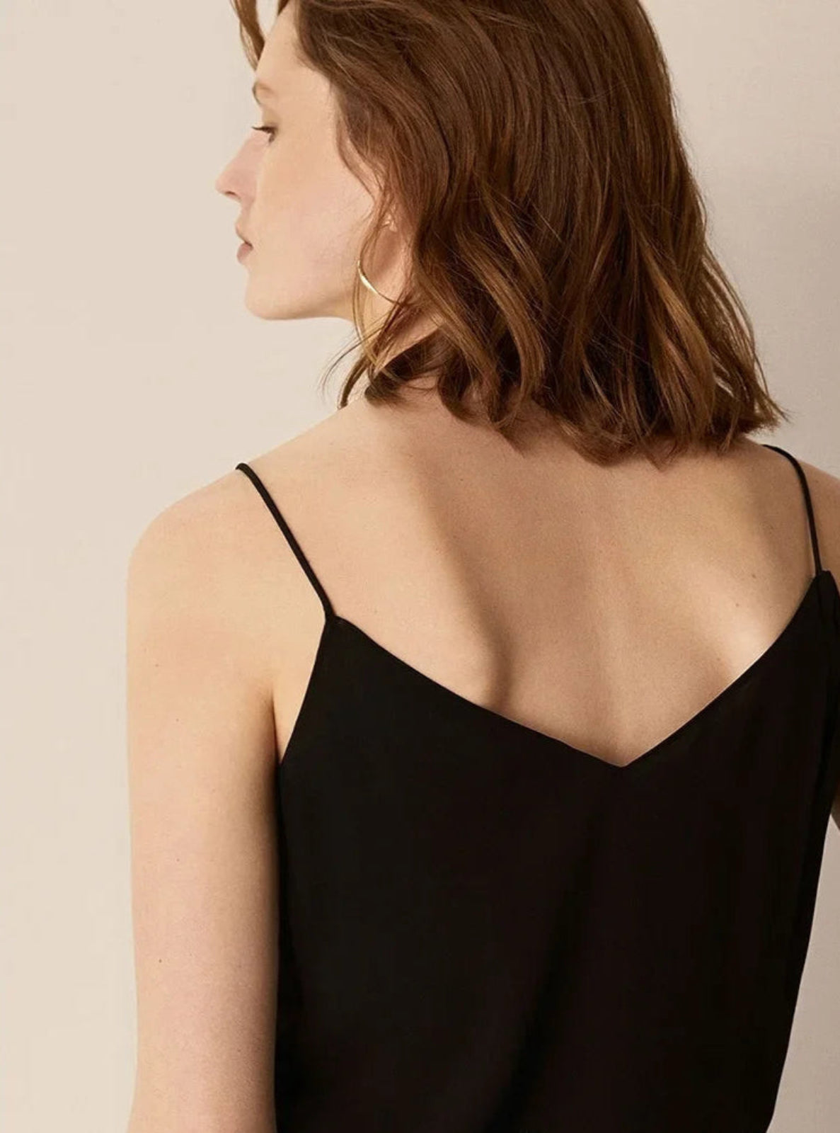 Woman wearing a black spaghetti strap top against a beige background