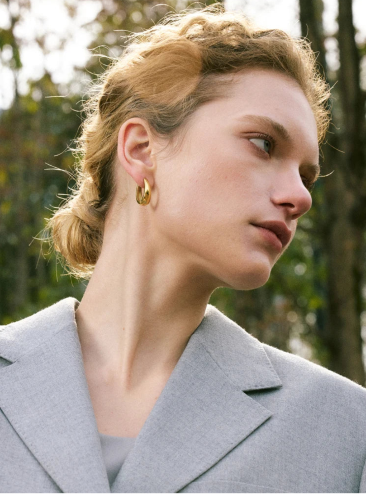 Woman wearing gold hoop earrings with a blurred natural background