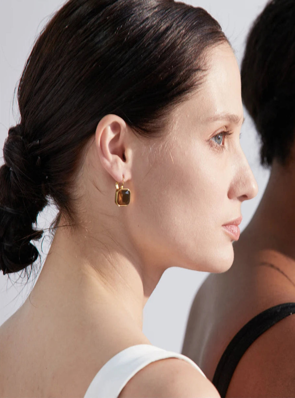 Close-up of a woman wearing a gold earring with a clear gemstone.