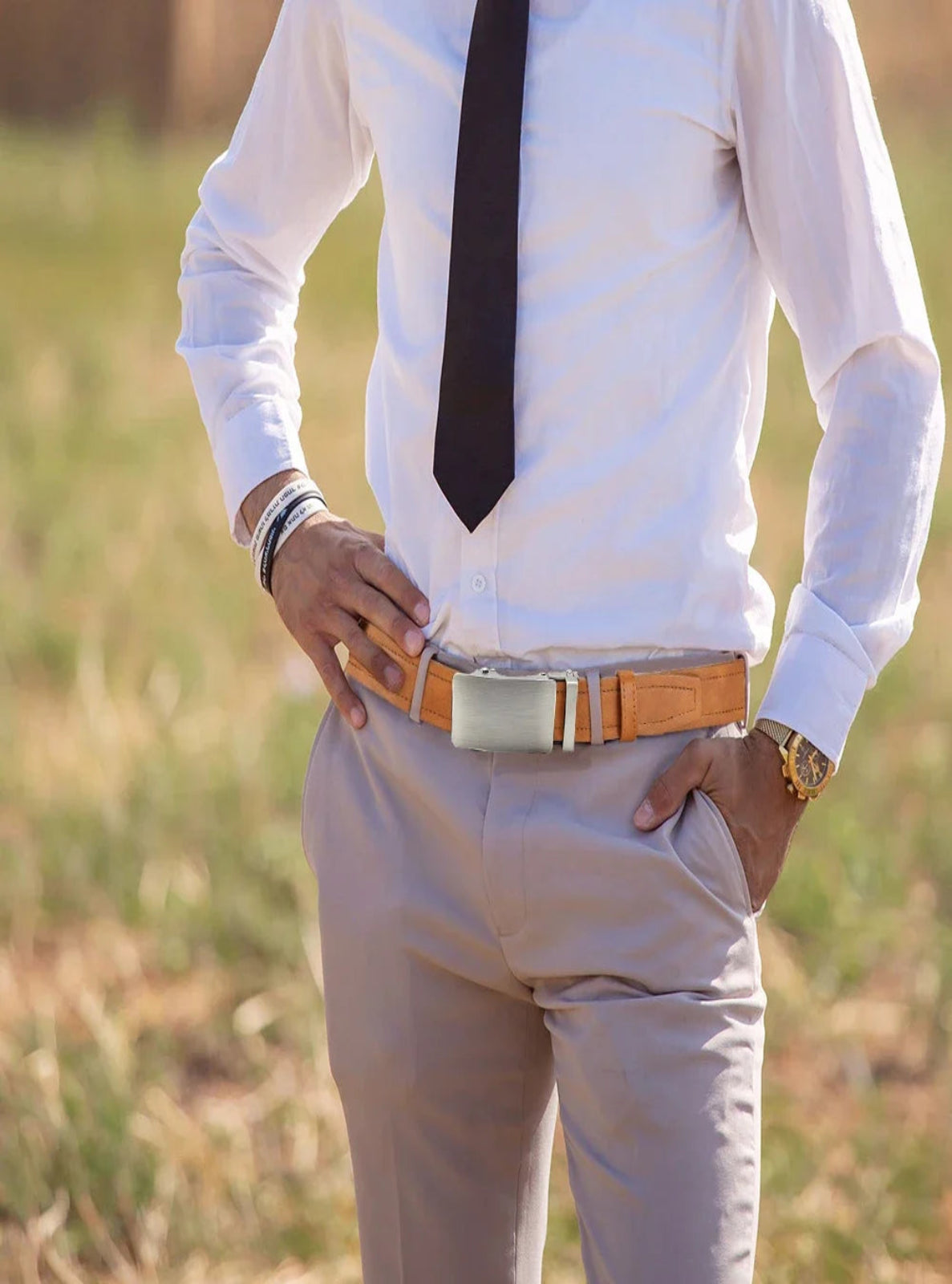 Person wearing a white shirt, beige pants, and a brown belt with a blurred natural background