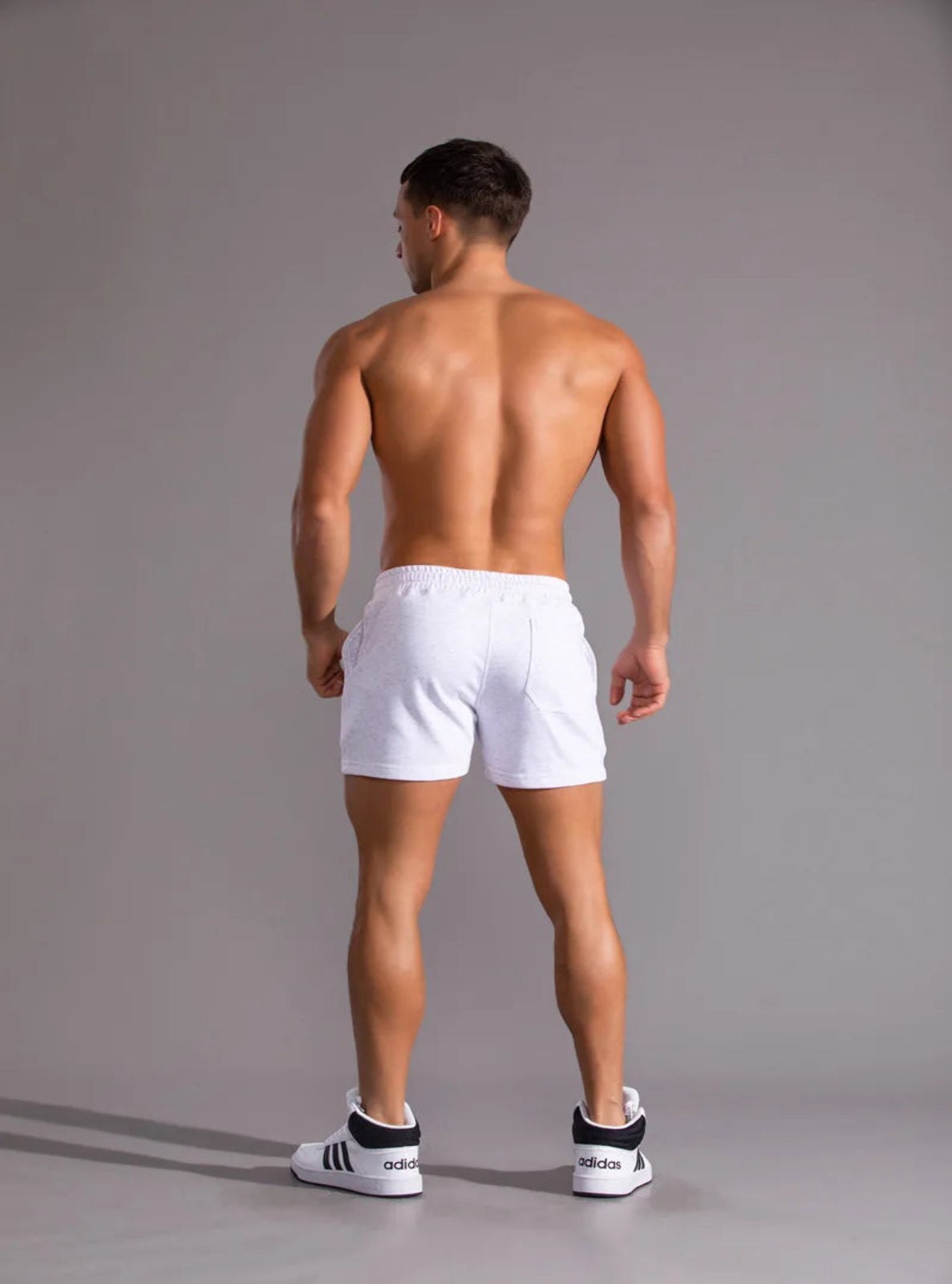 Man wearing white shorts standing against a gray background