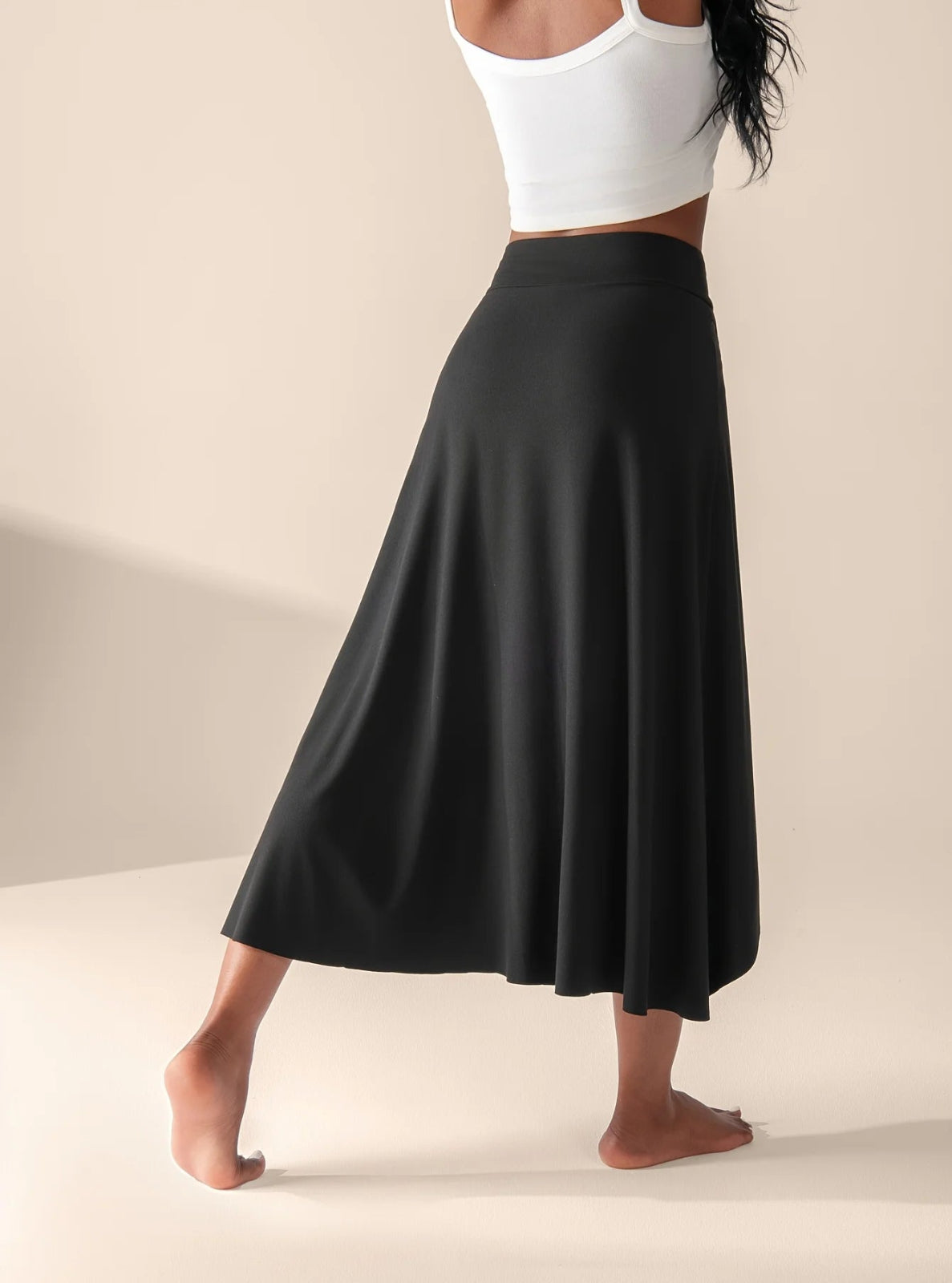 Person wearing a black skirt and white top on a neutral background