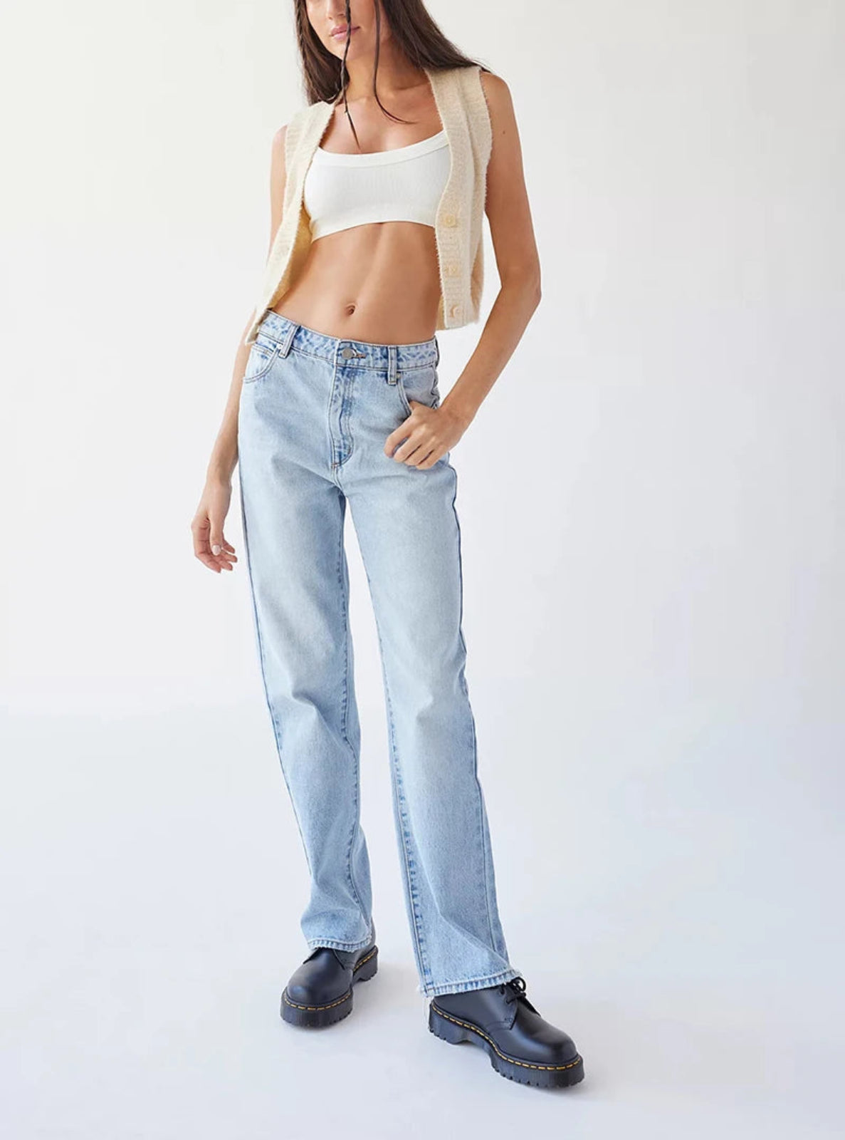 Person wearing light blue jeans and a white crop top on a plain background