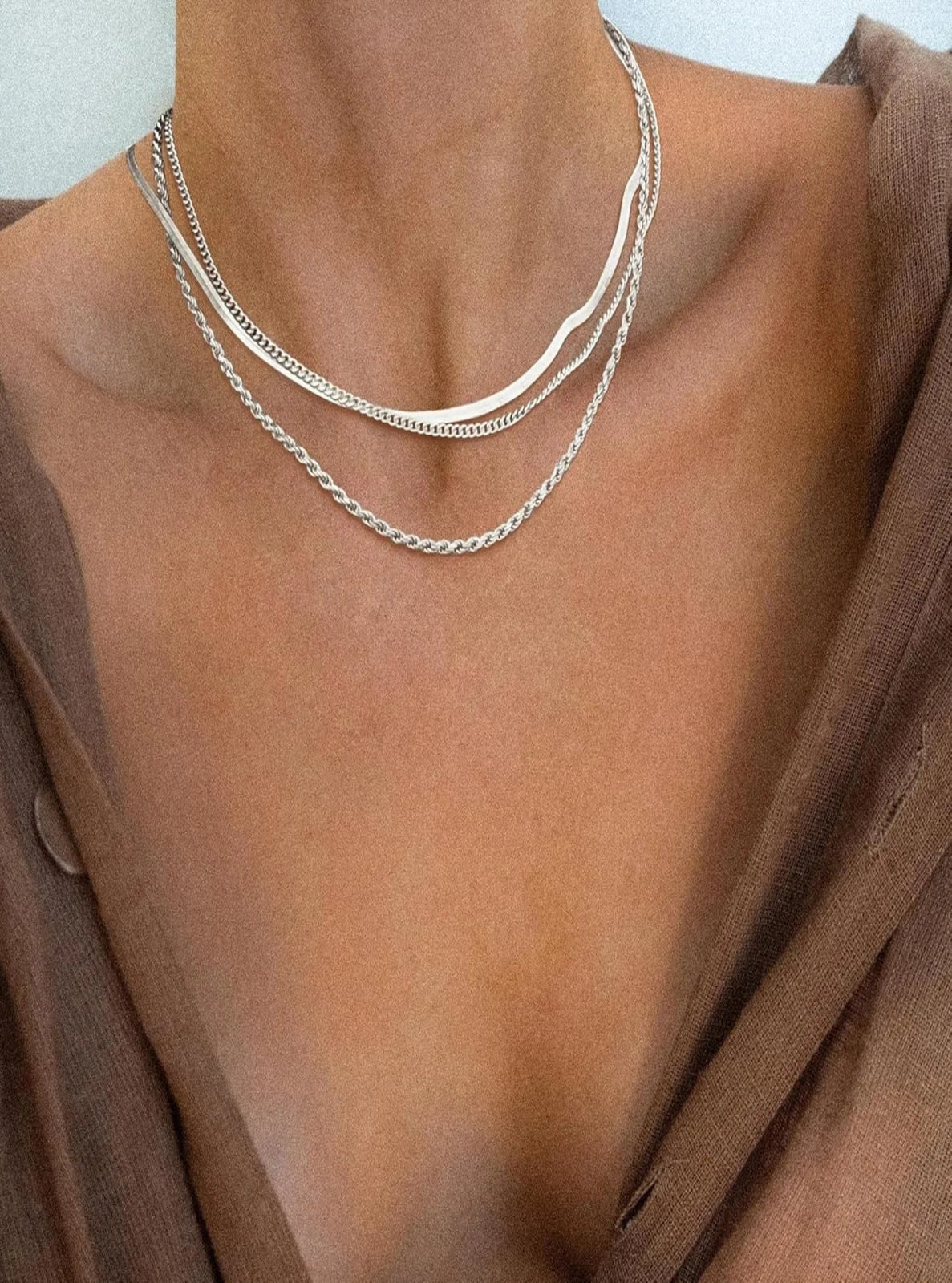 Silver necklaces on a person wearing a brown garment