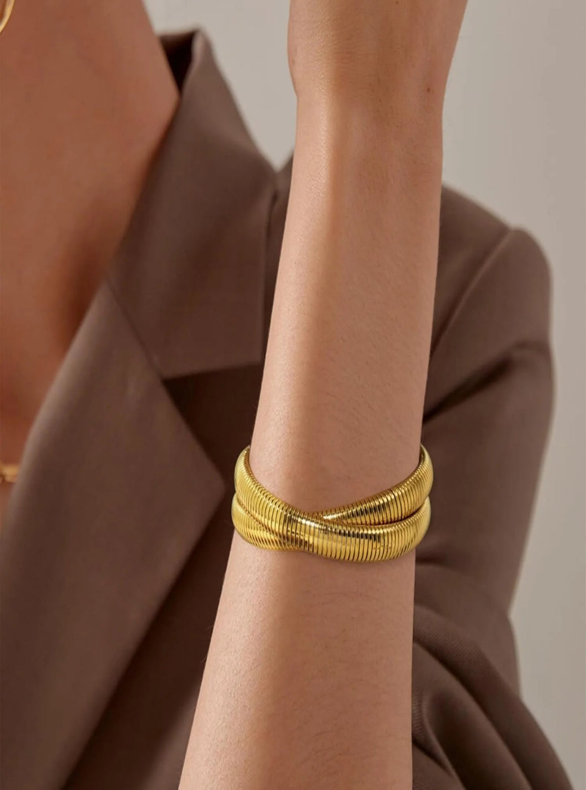 Gold bracelet on a wrist with a brown garment in the background