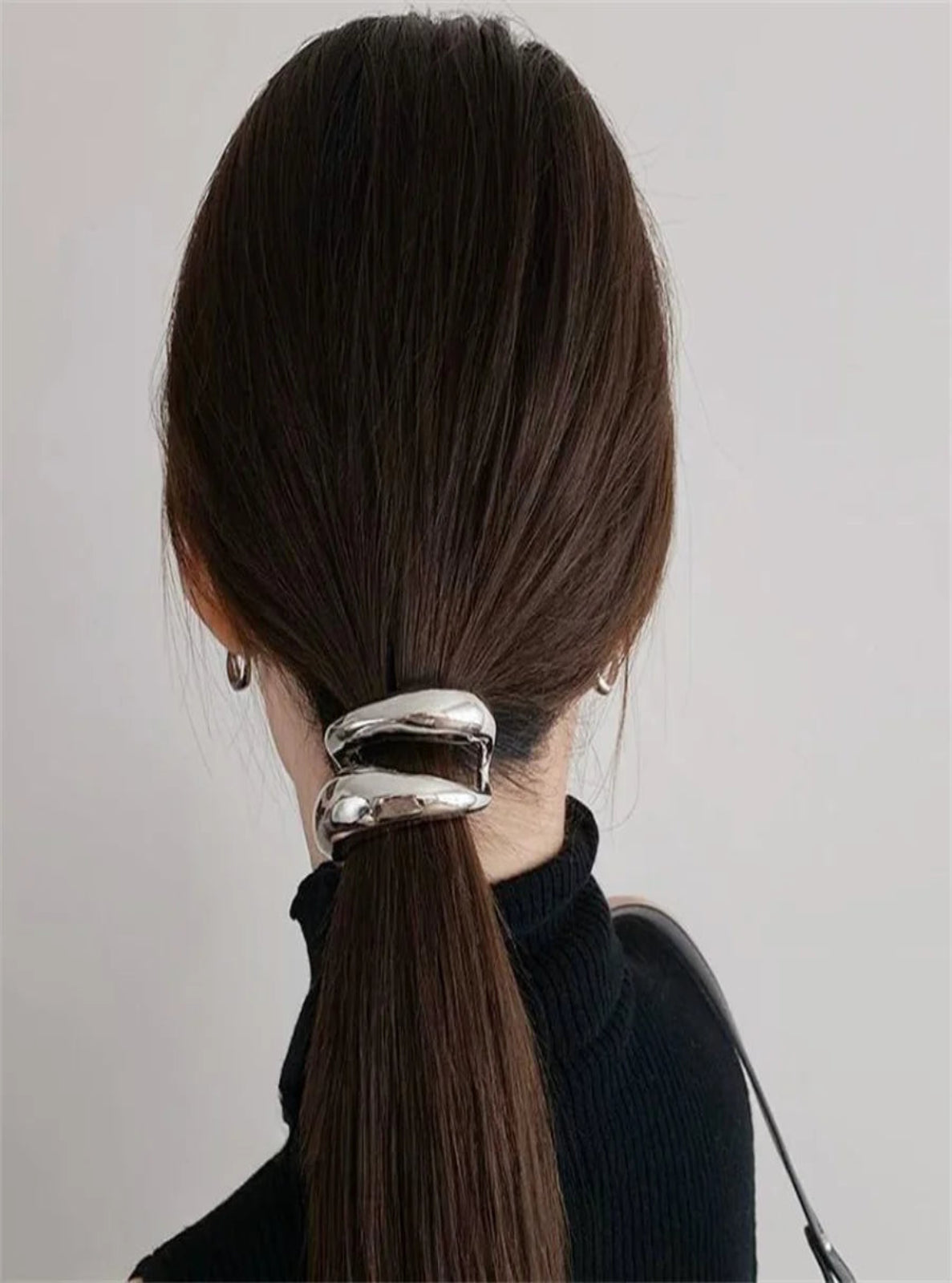 Person with a ponytail held by a silver hair tie against a plain background
