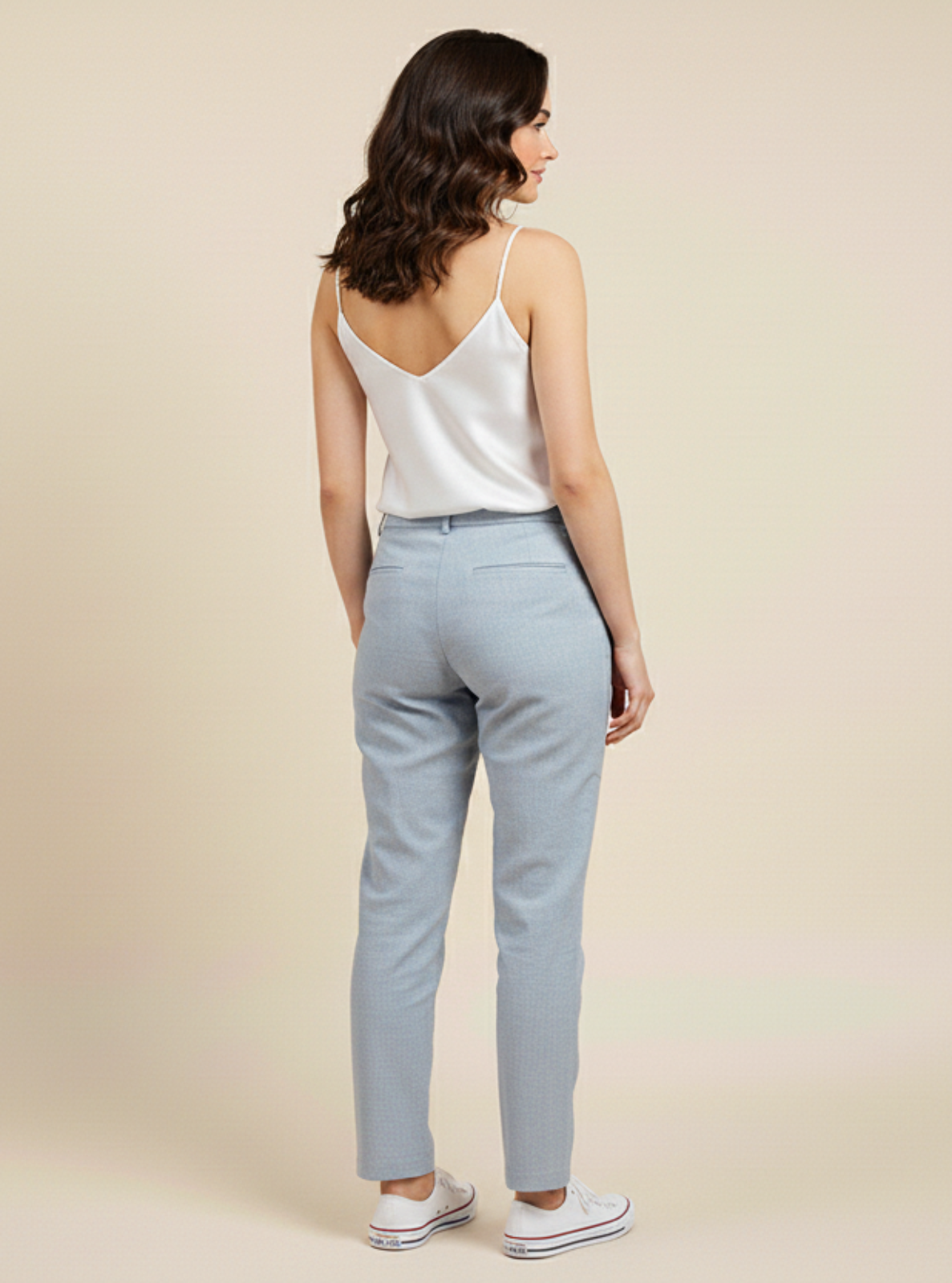 Woman wearing a white top and light gray pants on a beige background