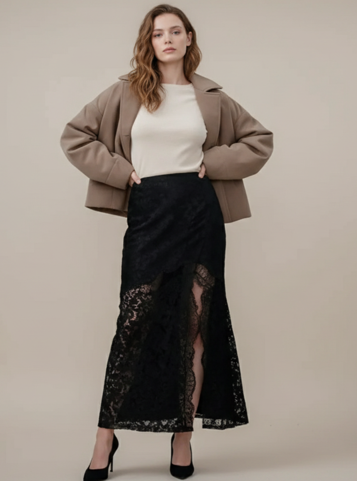 Woman wearing a beige jacket, white top, and black lace skirt on a plain background