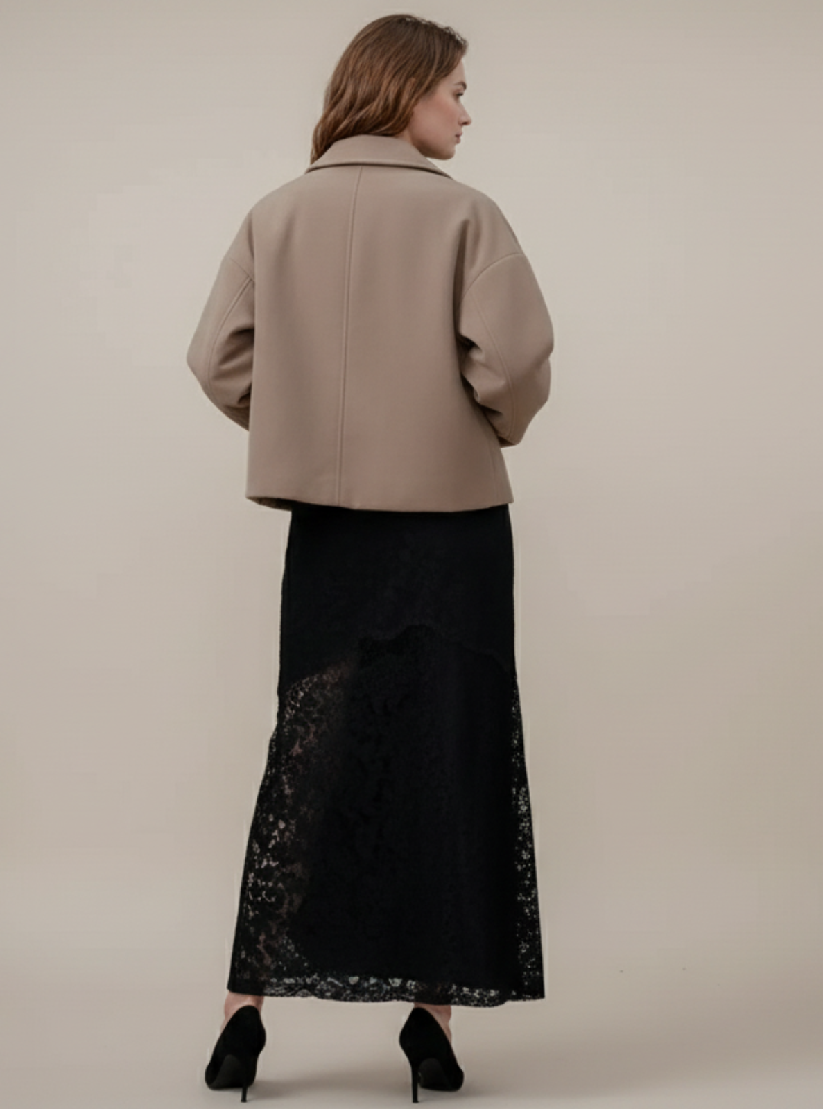 Woman wearing a beige coat and black skirt against a plain background