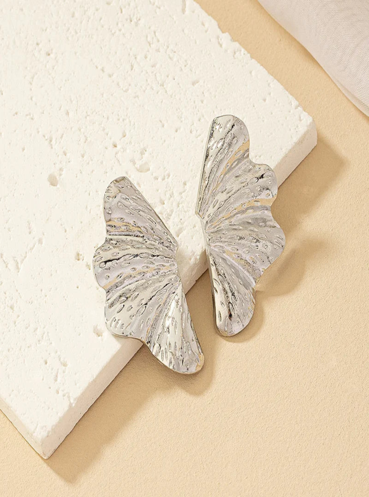 Silver earrings on a textured beige surface