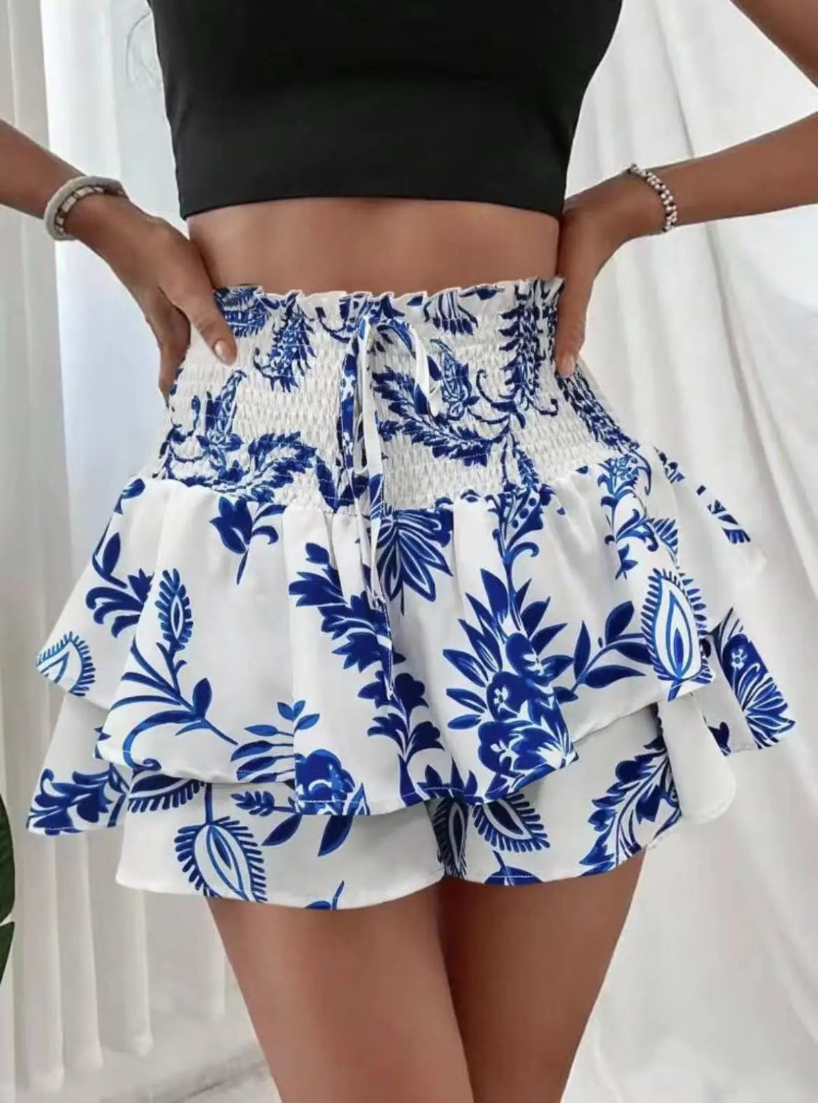 Person wearing a black top and blue floral white shorts against a white background