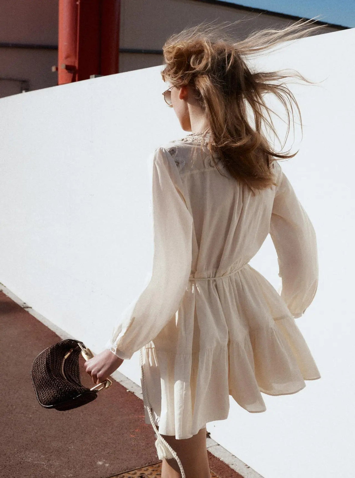 Woman in a white dress with a brown bag standing on a rooftop with a clear sky.