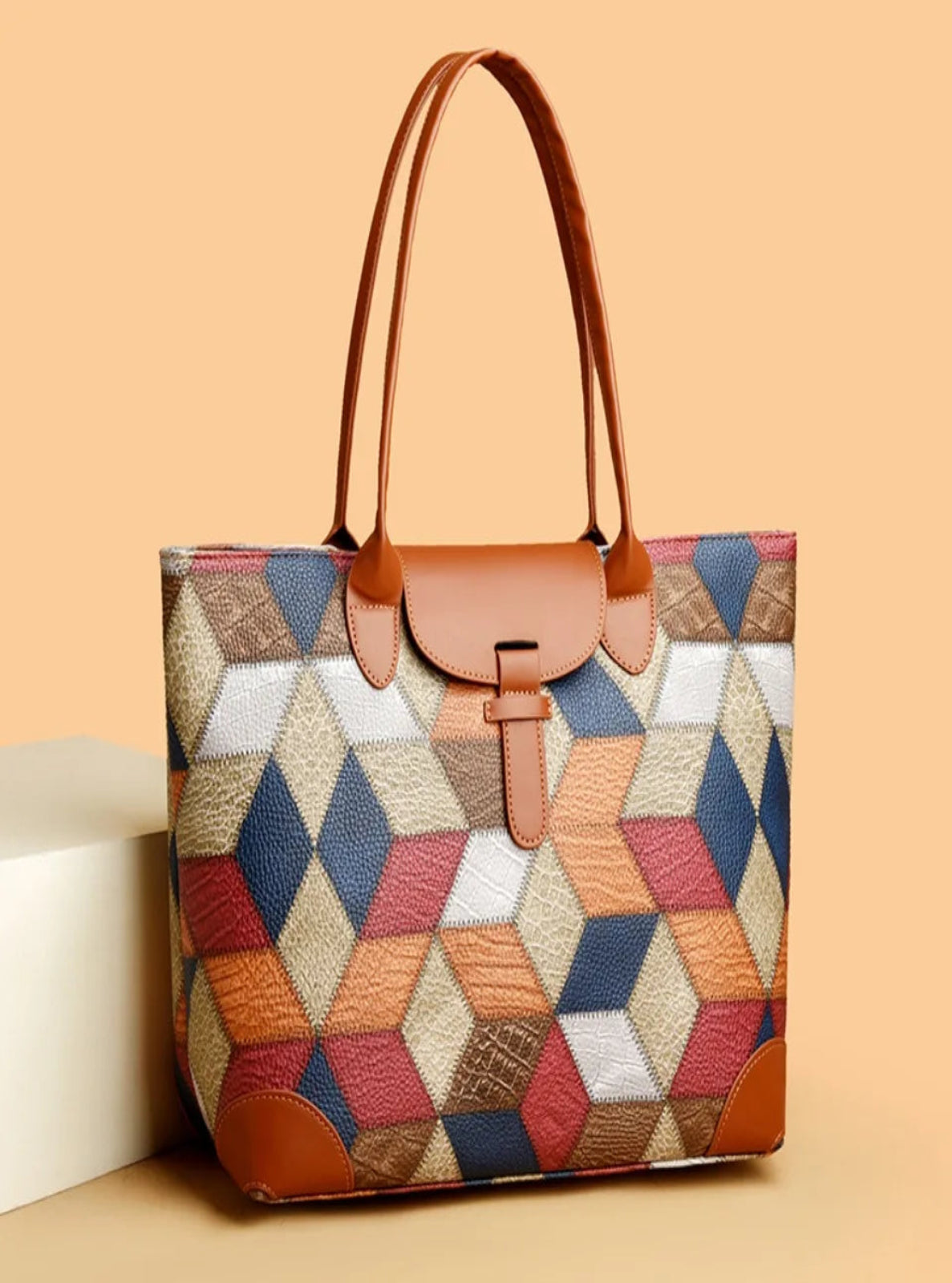 Multicolored geometric patterned handbag with brown leather accents on a beige background