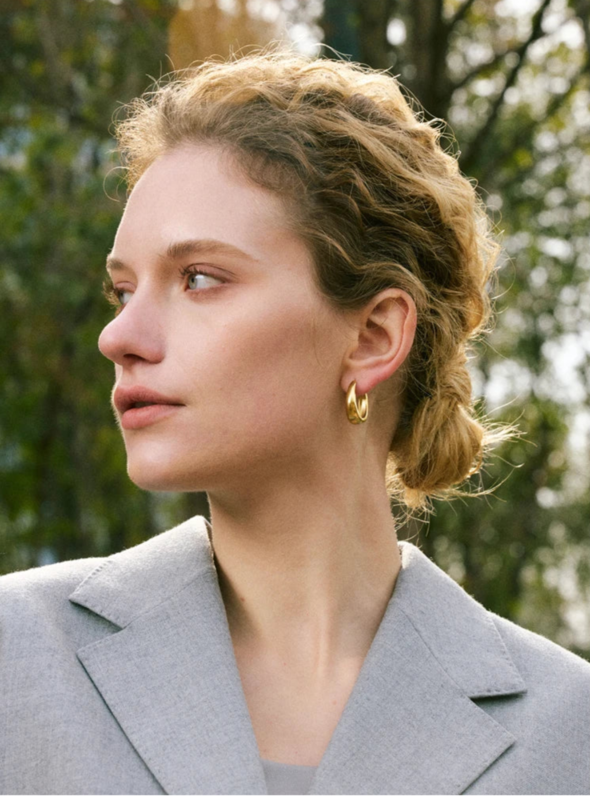 Woman wearing a gray blazer with a blurred natural background